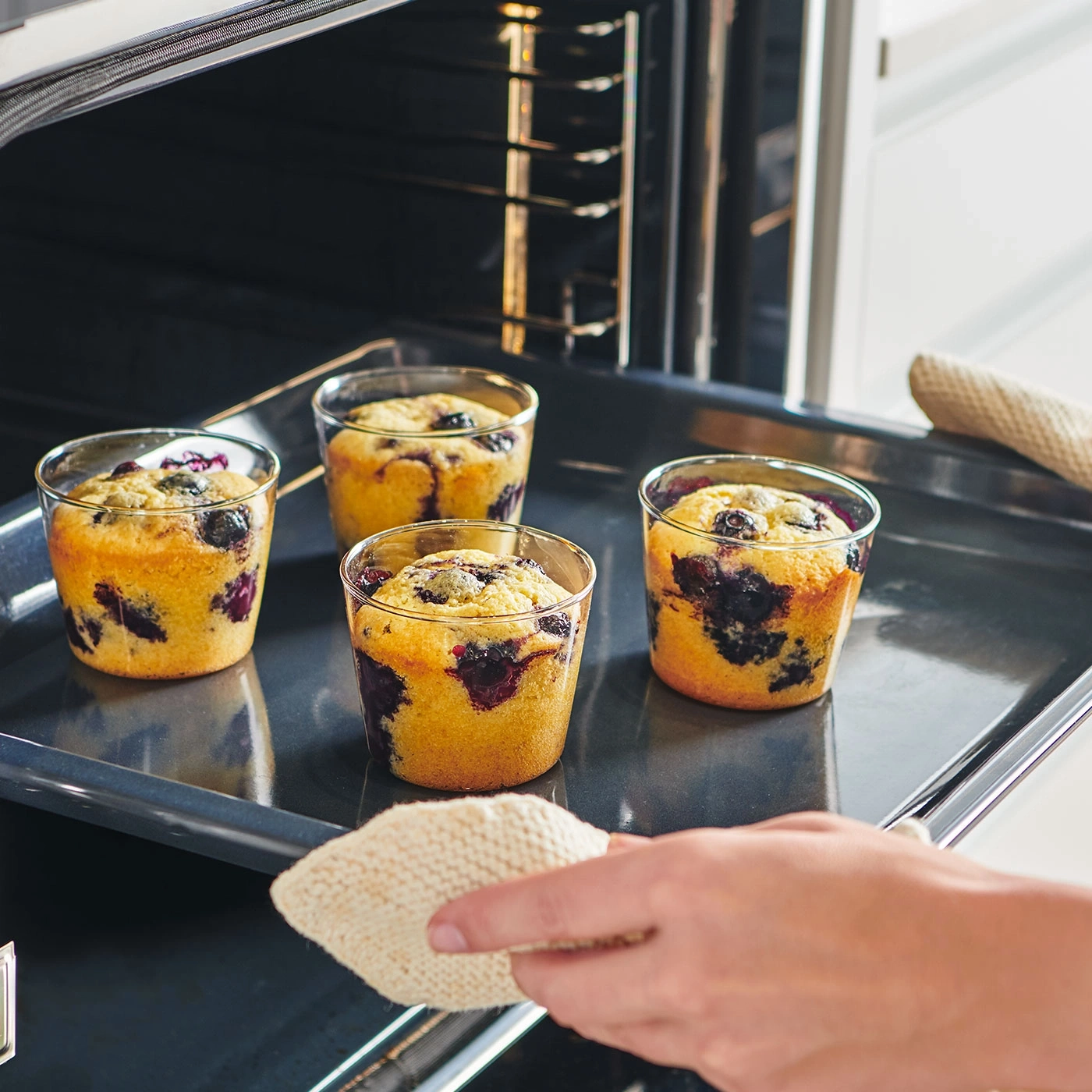Muffins aux myrtilles dans le four, sur une plaque, avec un gant de cuisine.