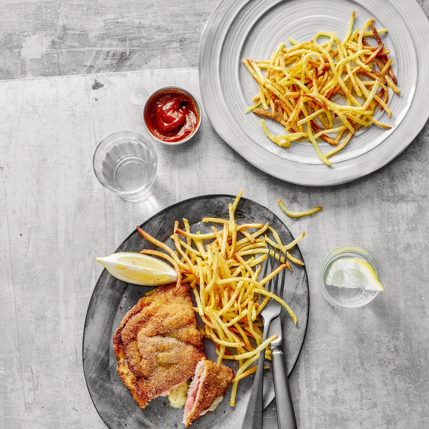Escalope avec frites, ketchup, citron et boissons sur une table