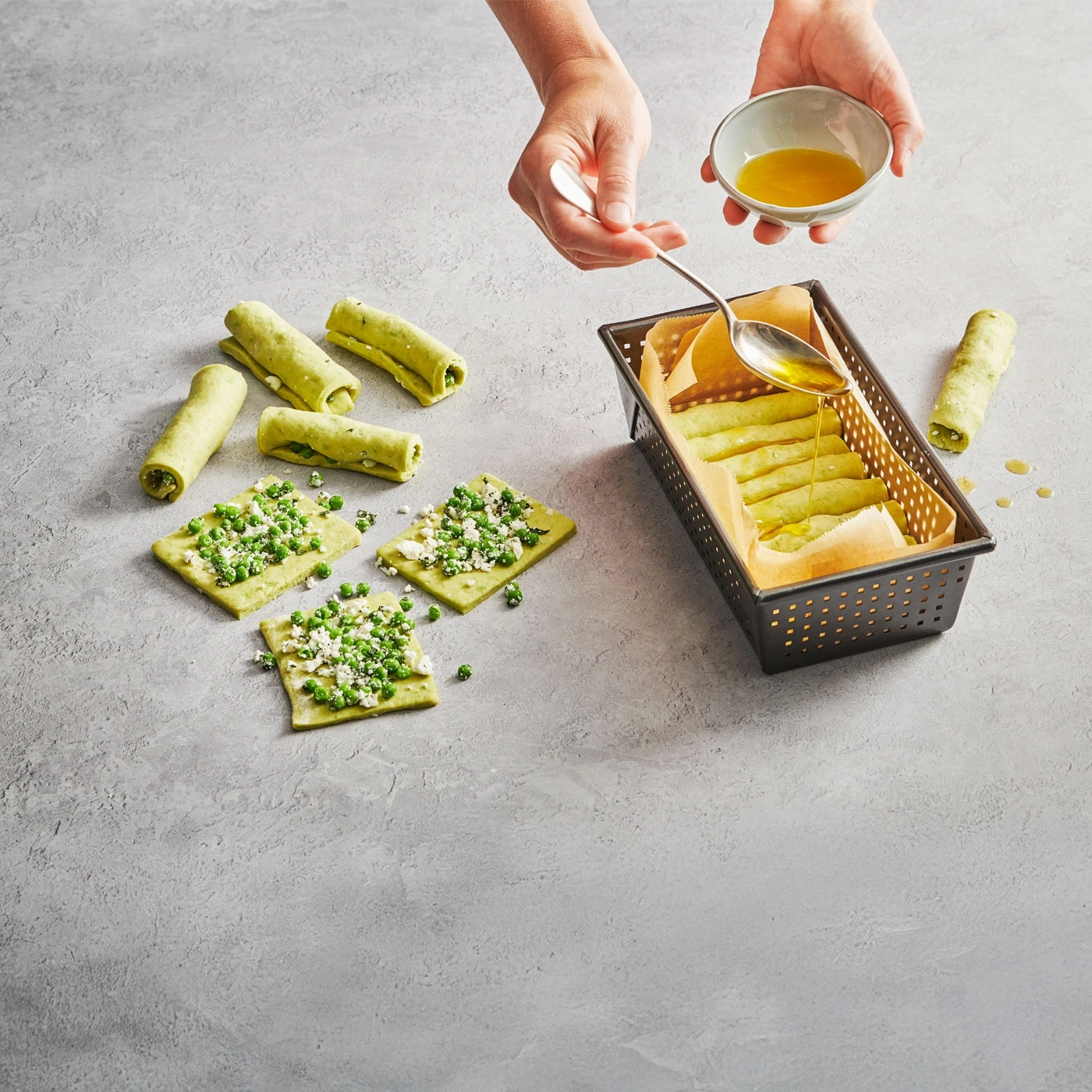 Rouleaux de pâtes vertes avec des pois et du fromage, arrosés d'huile.