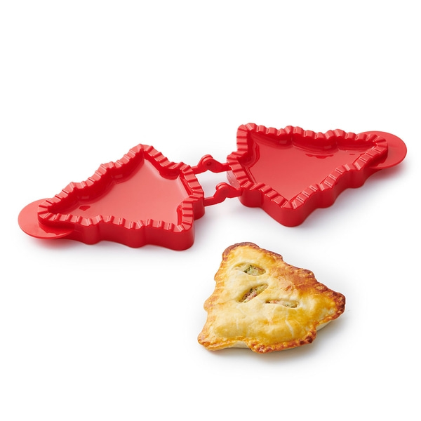 Roter Ausstecher und gebackenes Gebäck in Weihnachtsbaumform auf weißem Hintergrund.