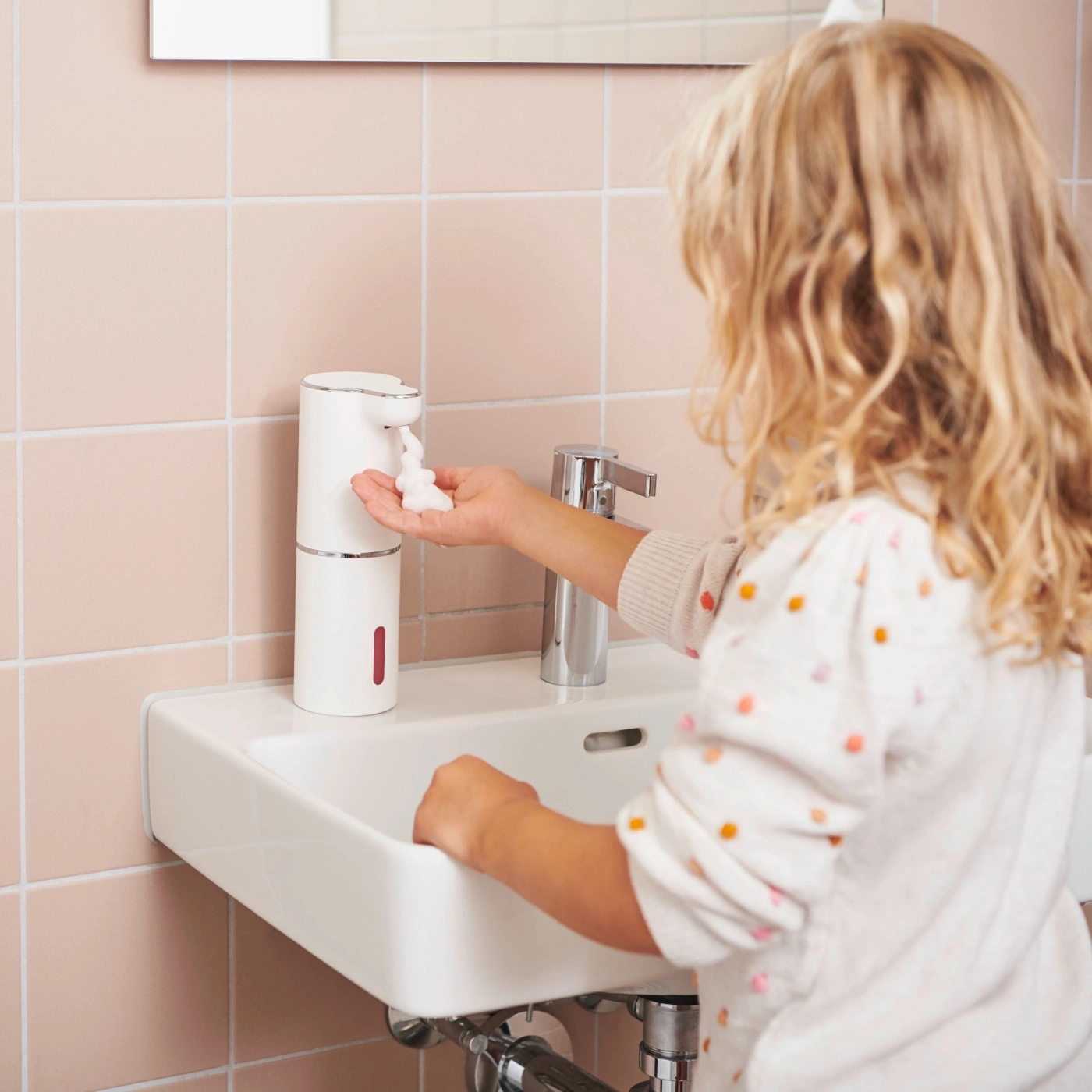Enfant utilise un distributeur de savon dans la salle de bain pour se laver les mains.