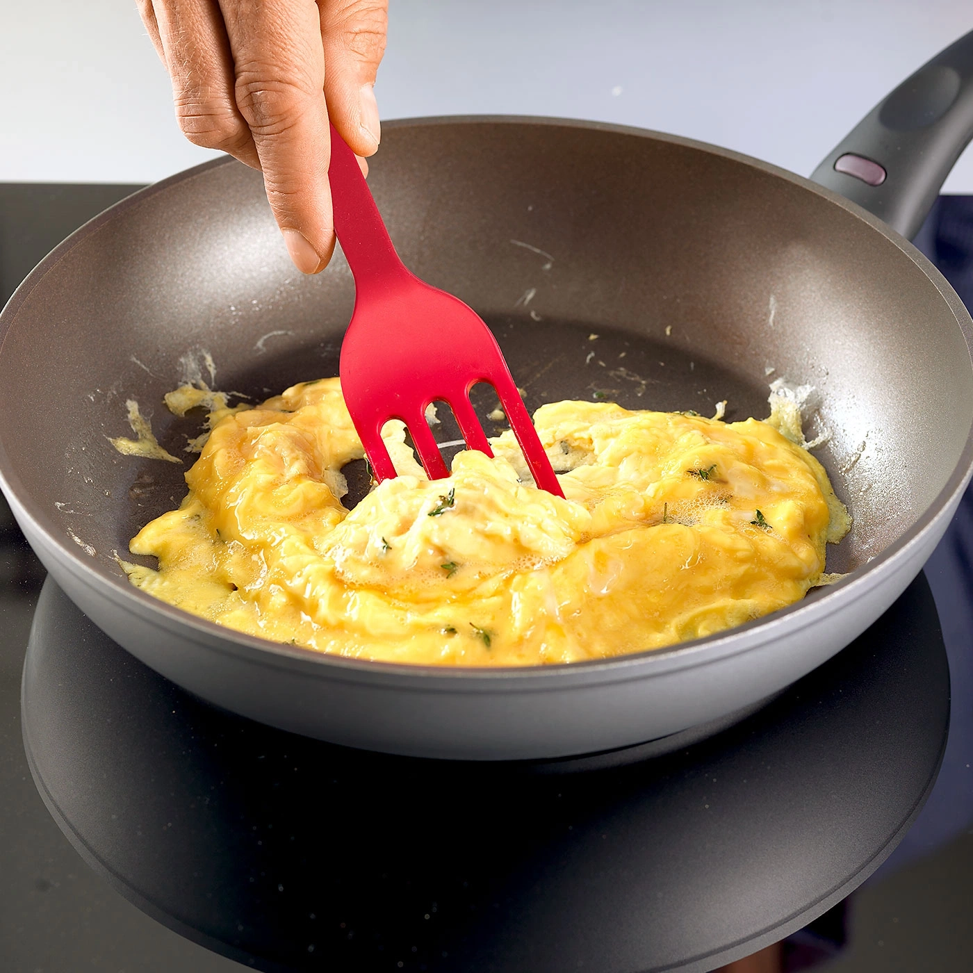 Person rührt Rührei in einer Pfanne mit einem roten Spatel.