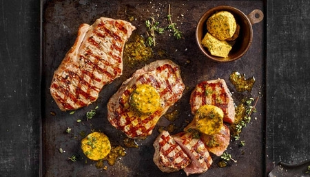 Gegrillte Steaks mit Kräuterbutter und Kräutern auf einem Tablett