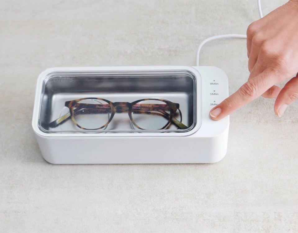 Brille in einem Ultraschallreiniger. Person drückt die 3-Minuten-Taste.
