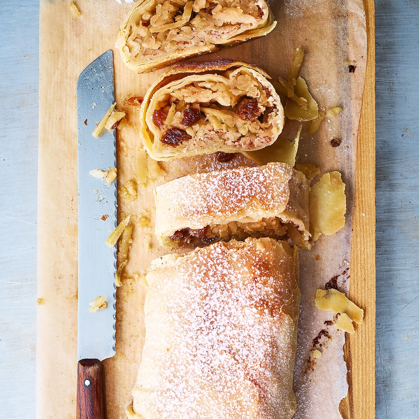 Apfelstrudel auf Holzbrett mit Messer und Puderzucker, Ansicht von oben