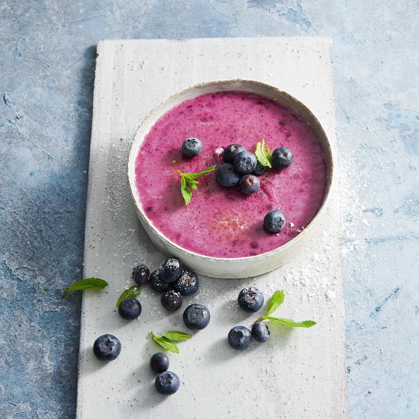 Blaubeersuppe mit Blaubeeren und Minze auf einem weißen Brett