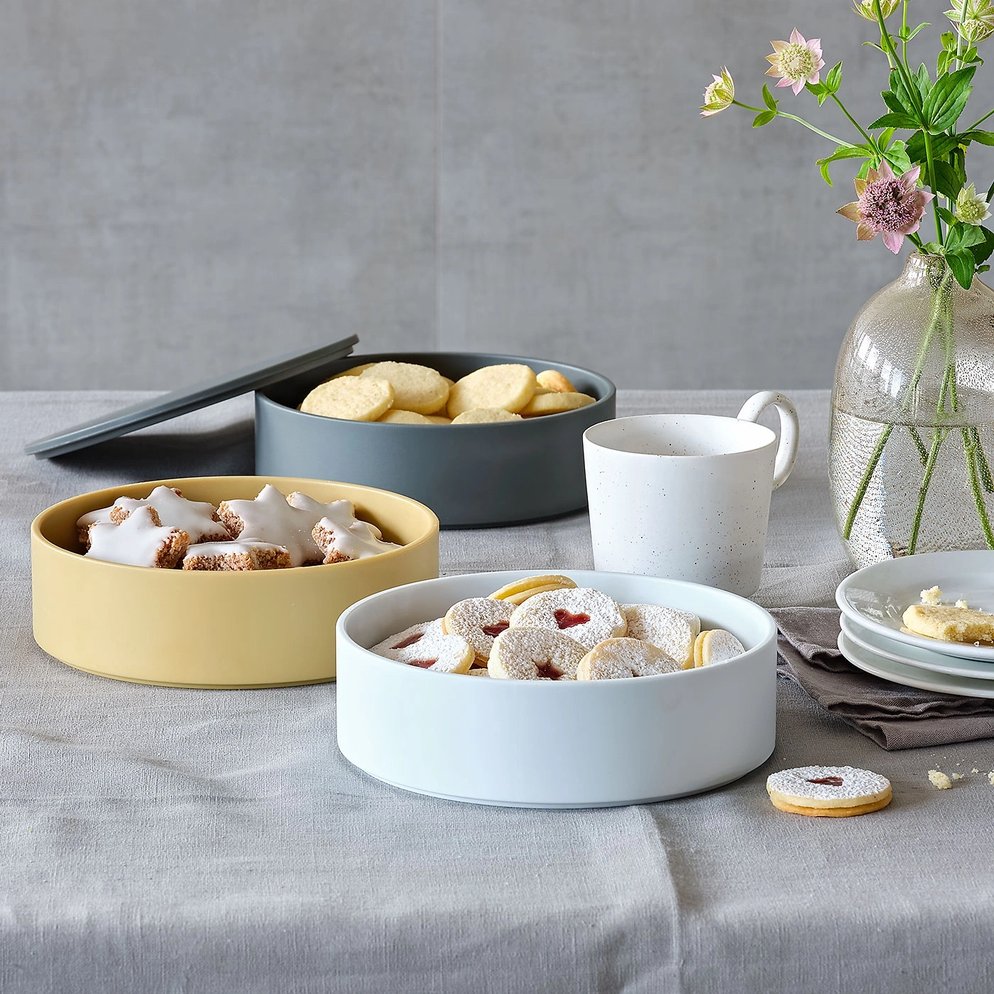 Kekse in Schalen, Tasse, Vase mit Blumen, auf einem Tisch mit Stoffdecke.