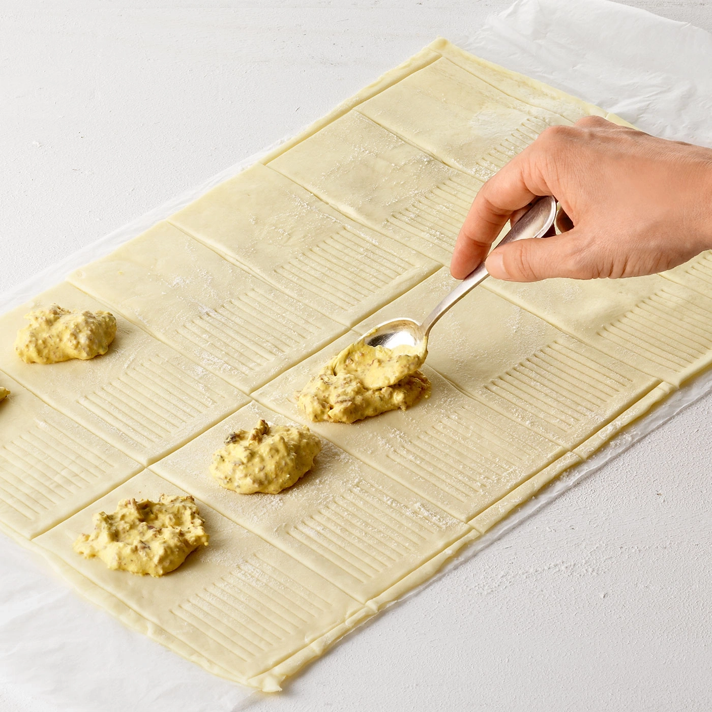 Main avec une cuillère qui dépose une garniture sur de la pâte feuilletée, gros plan