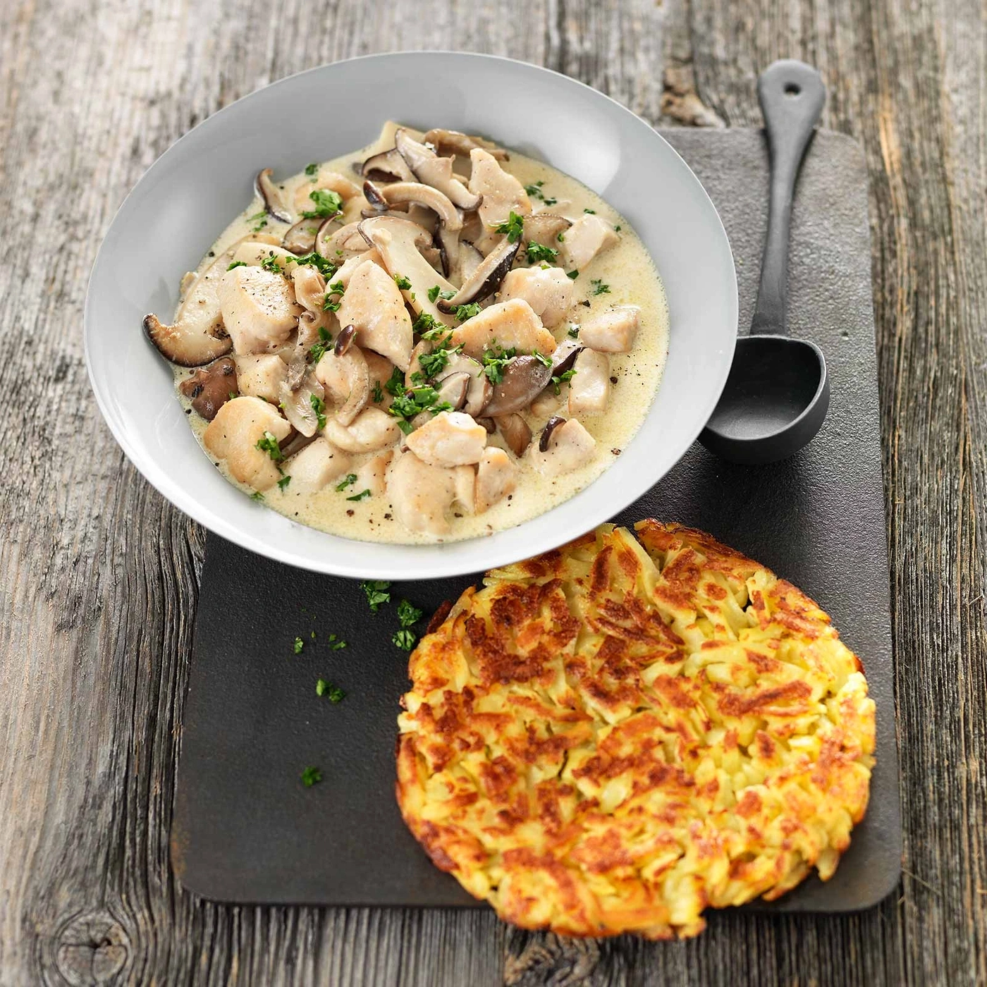 Hühnchen-Pilz-Ragout mit Rösti auf Holzbrett, lecker und appetitlich
