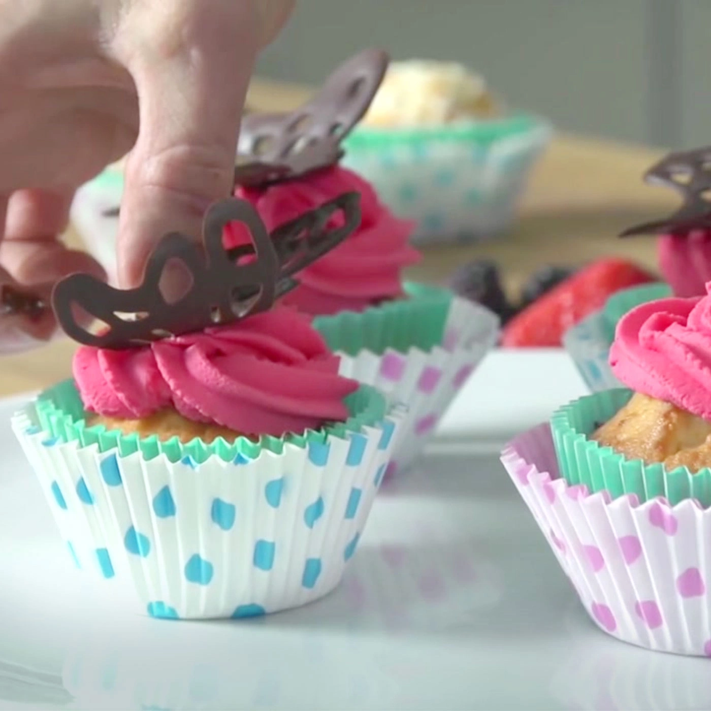 Cupcakes avec crème rose et décoration papillon sur une assiette.