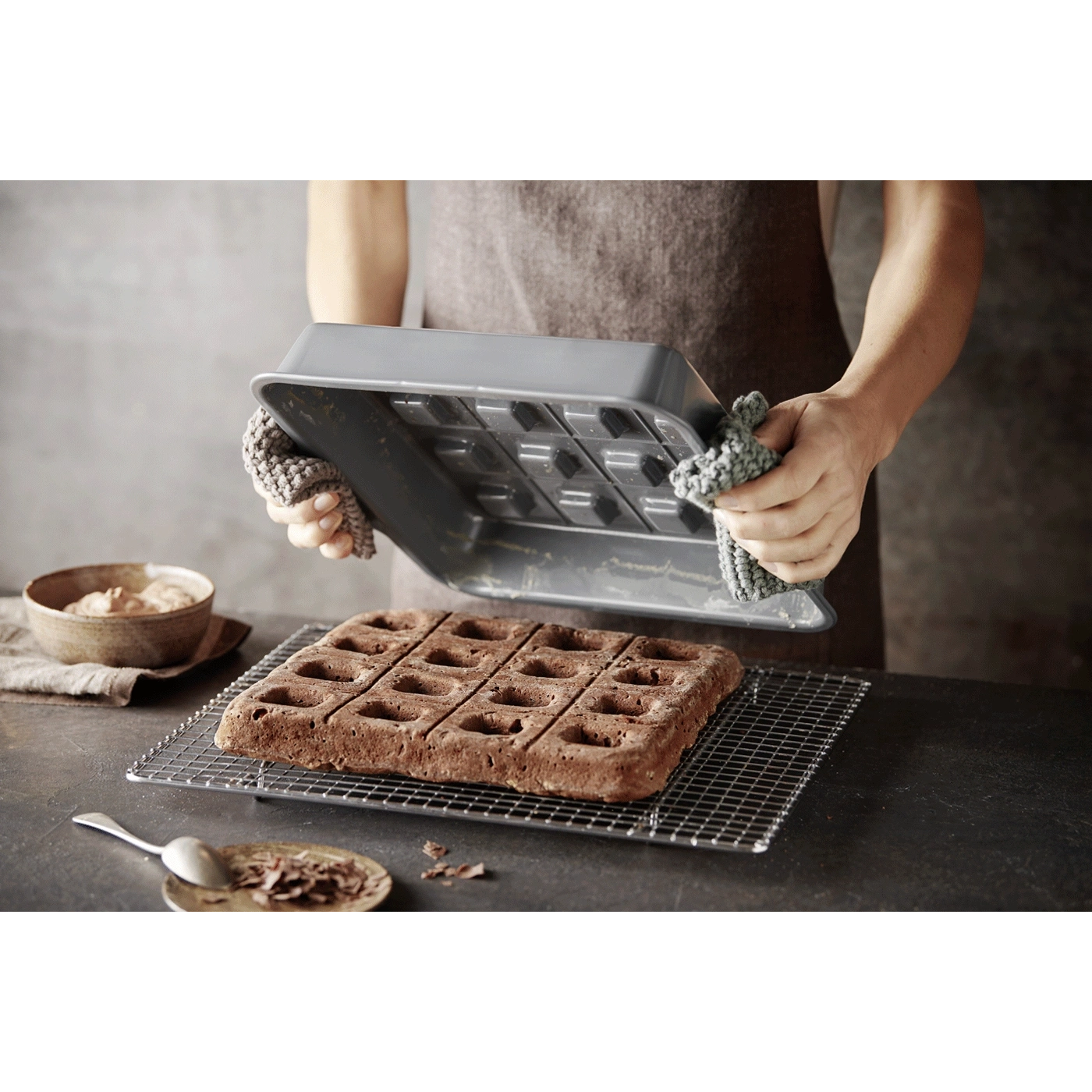 Person hält Backform über Kuchen auf einem Rost, mit Schokoladenstückchen.