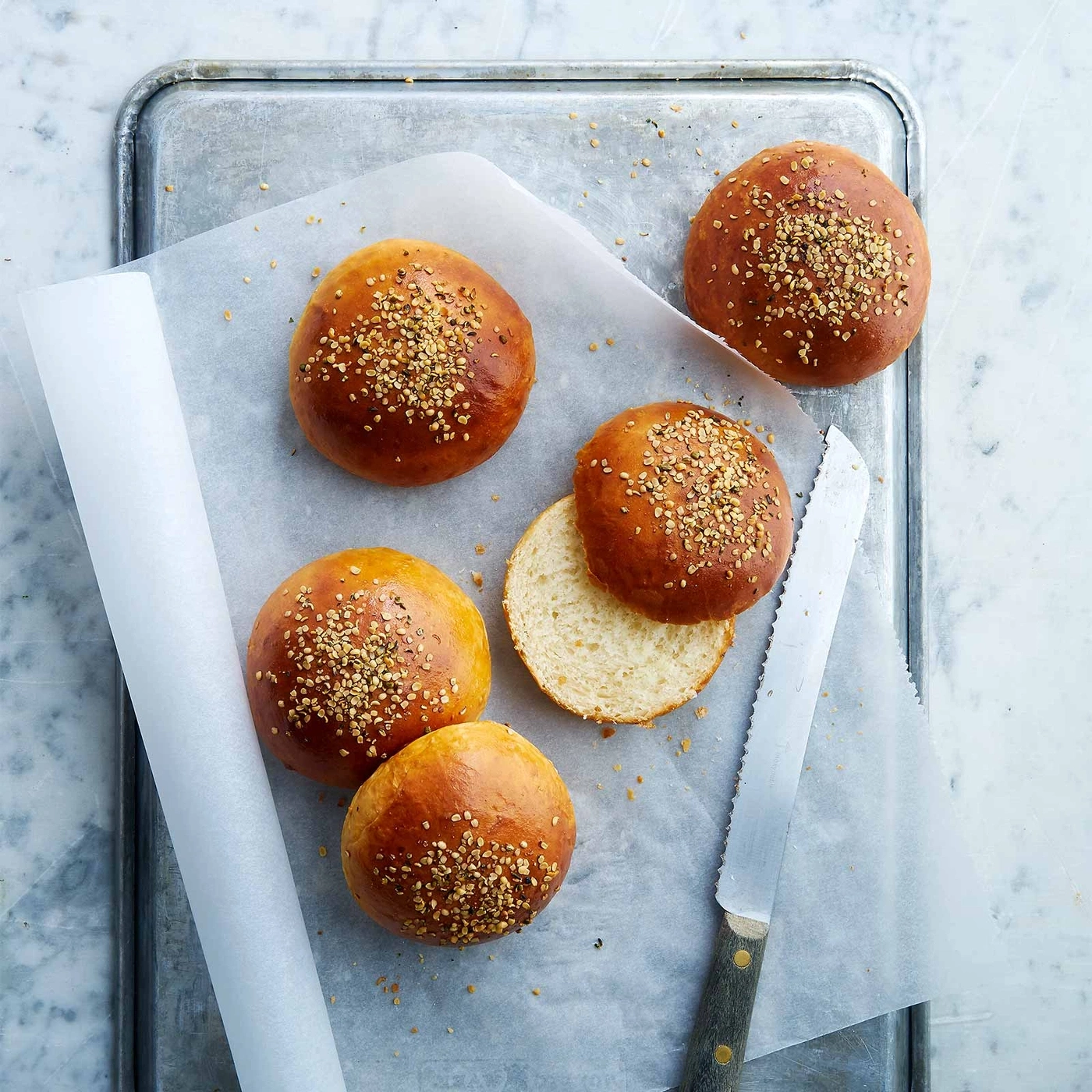 Burgerbrötchen auf Backpapier auf einem Tablett mit einem Messer