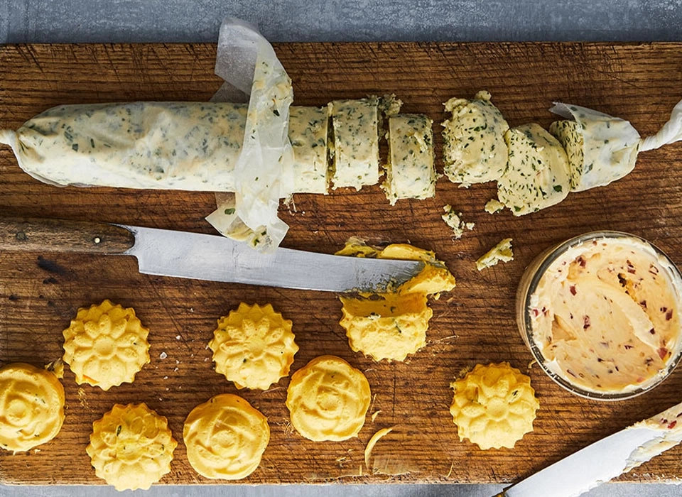 Holzbrett mit Kräuterbutter, Messer und Butterblumen-Keksen
