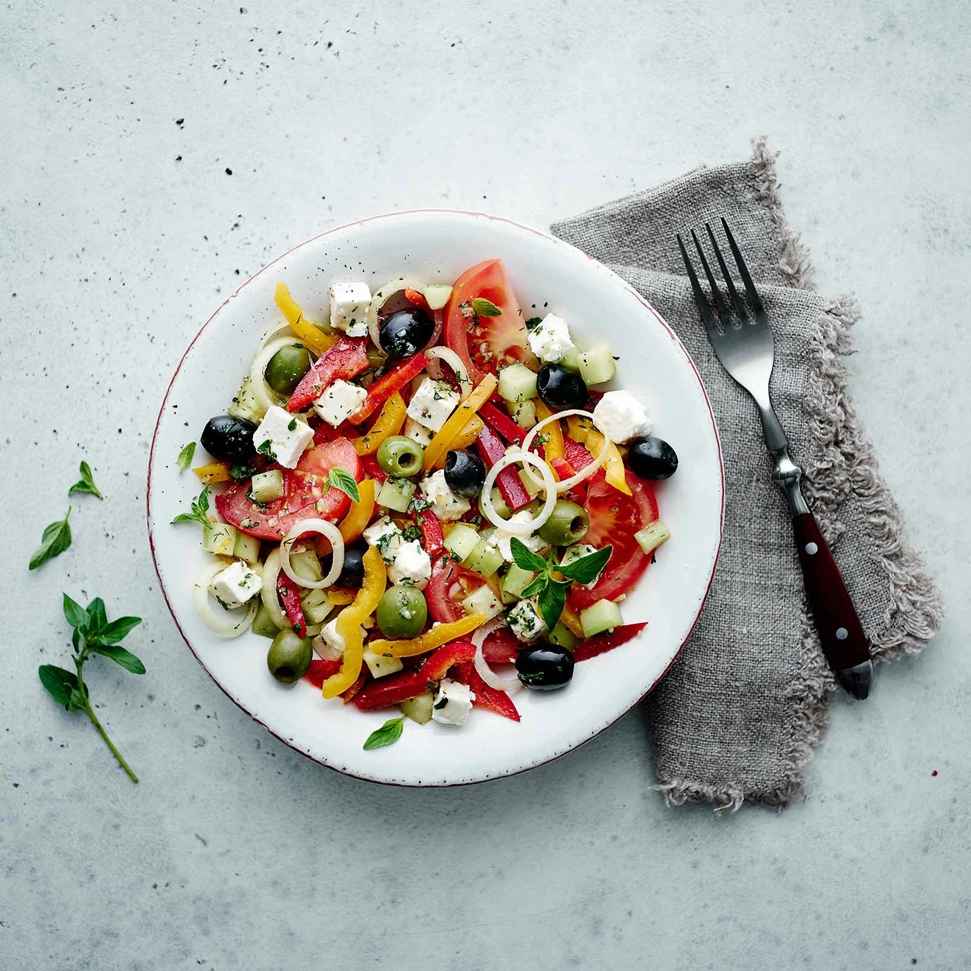Griechischer Salat auf einem Teller mit Oliven, Tomaten und Käse, mit einer Gabel.