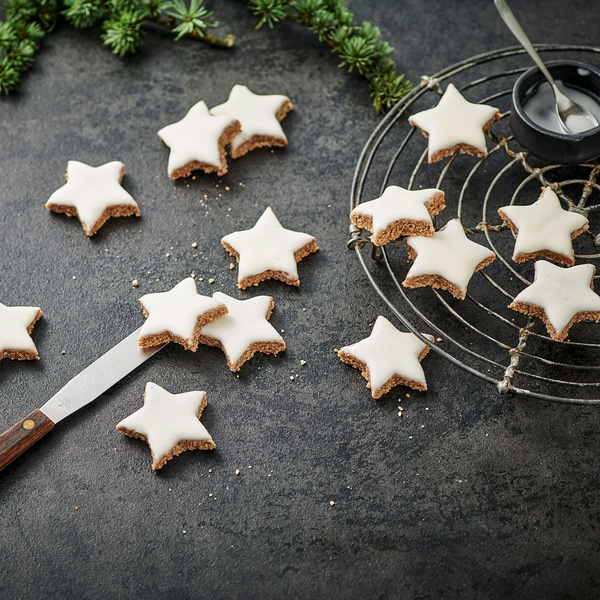 Sternförmige Kekse mit Zuckerguss auf dunklem Untergrund und Tannenzweig.