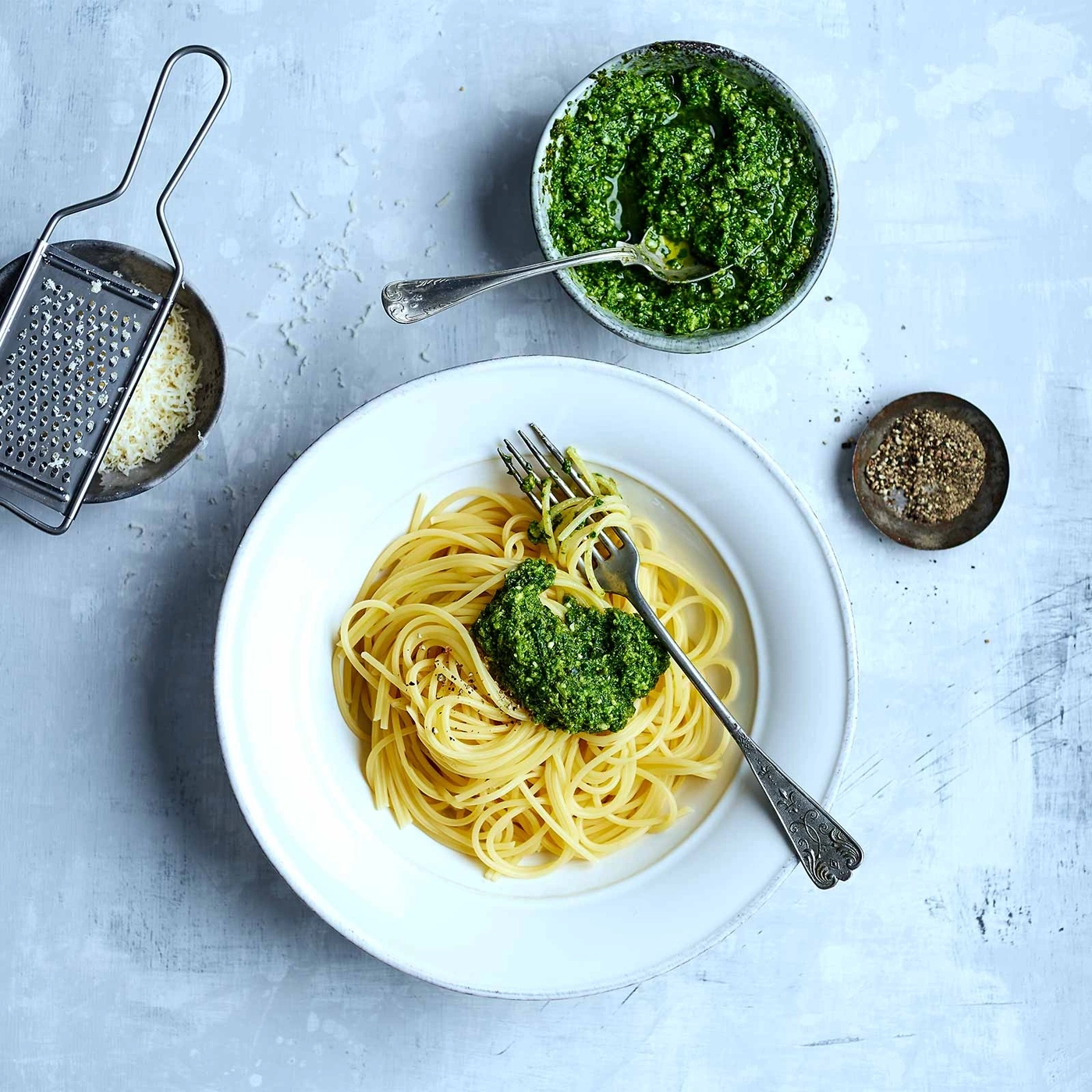 Spaghetti mit Pesto, Käse, Pfeffer und Utensilien auf einem Tisch
