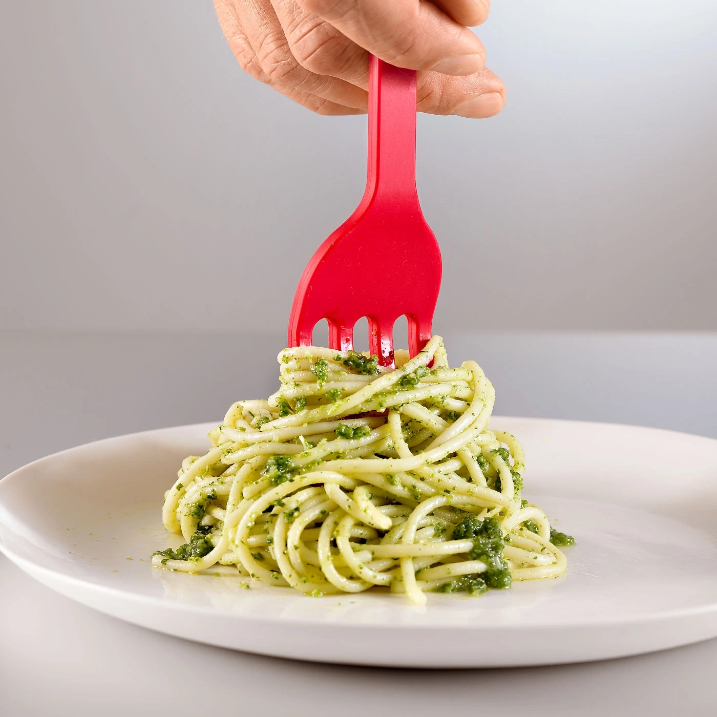 Ein Teller Spaghetti mit Pesto, gehalten von einer roten Gabel.