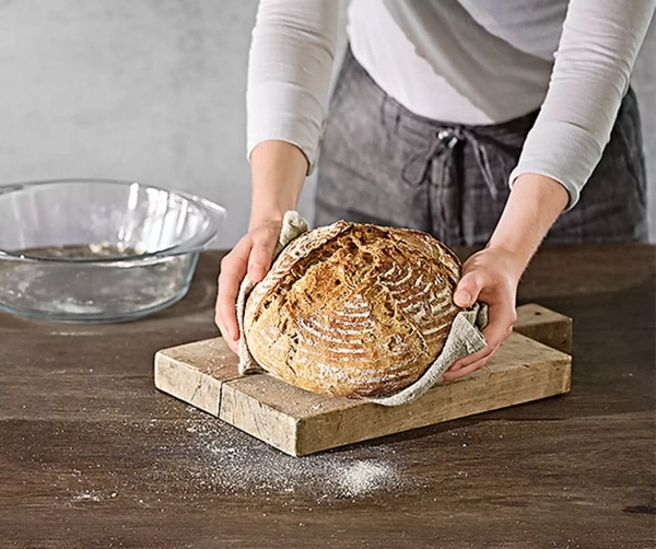 Eine Person hält ein frisch gebackenes Brot auf einem Holzbrett.