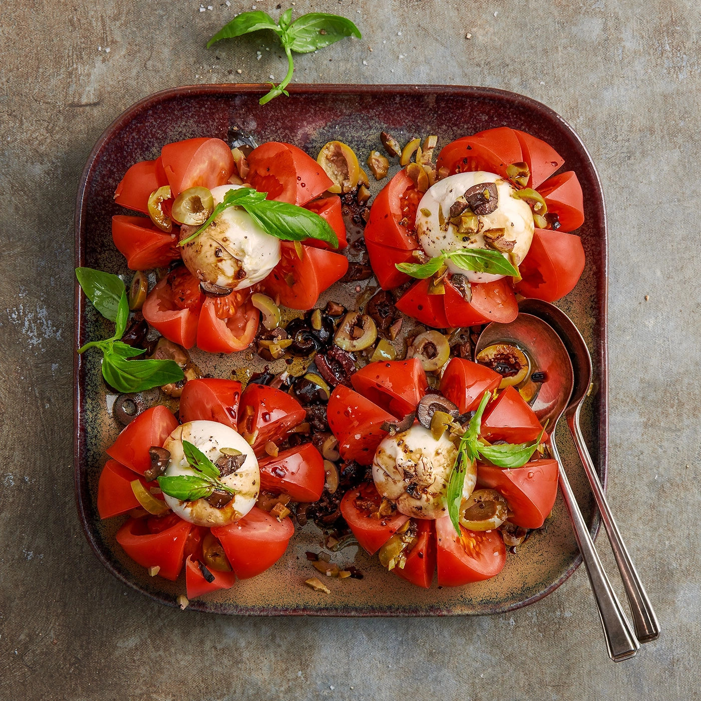 Tomaten-Burrata-Salat auf einem Teller mit Oliven und Basilikum