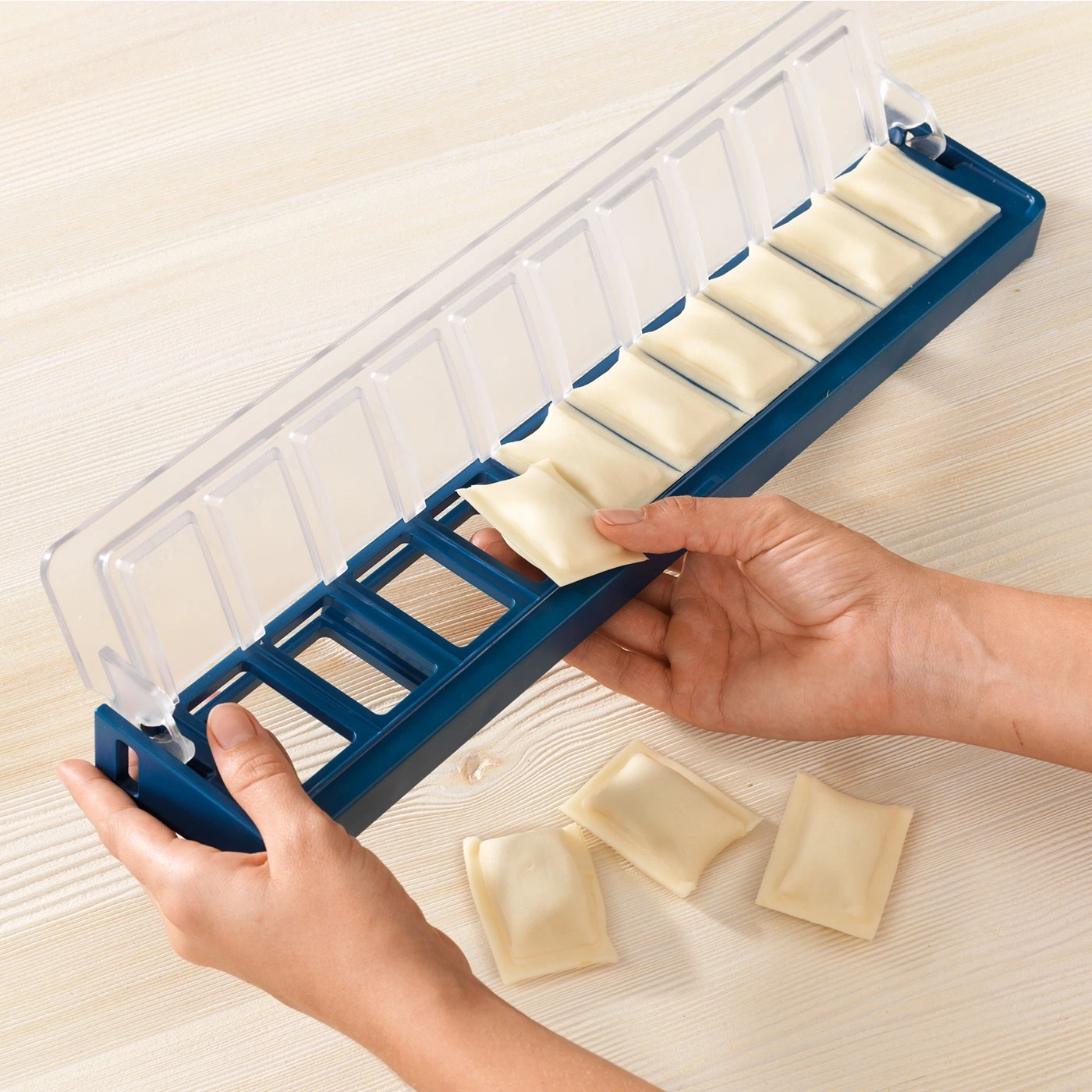 Fabricant de raviolis avec raviolis. Moule bleu, couvercle transparent, surface claire.