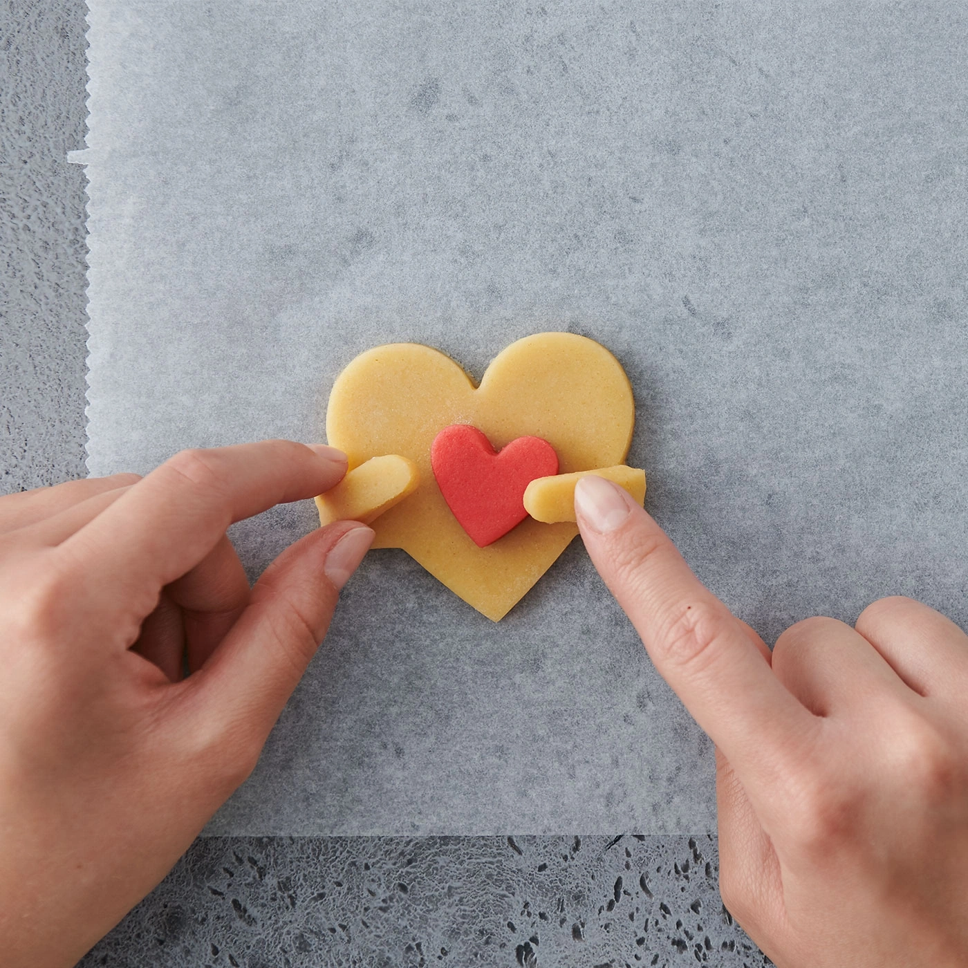 Mains façonnant des biscuits en forme de cœur sur du papier sulfurisé, gros plan, amour