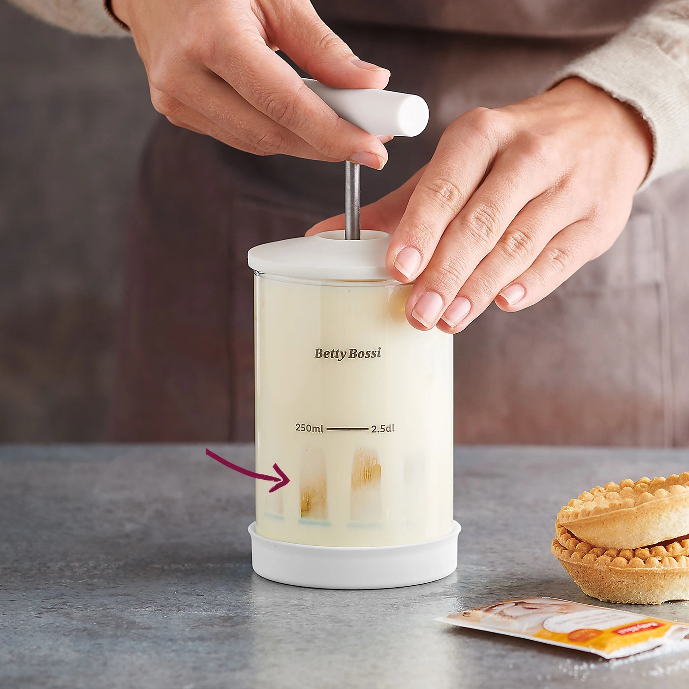 Person bereitet Creme in einem Behälter zu, mit Gebäck und Zutaten.