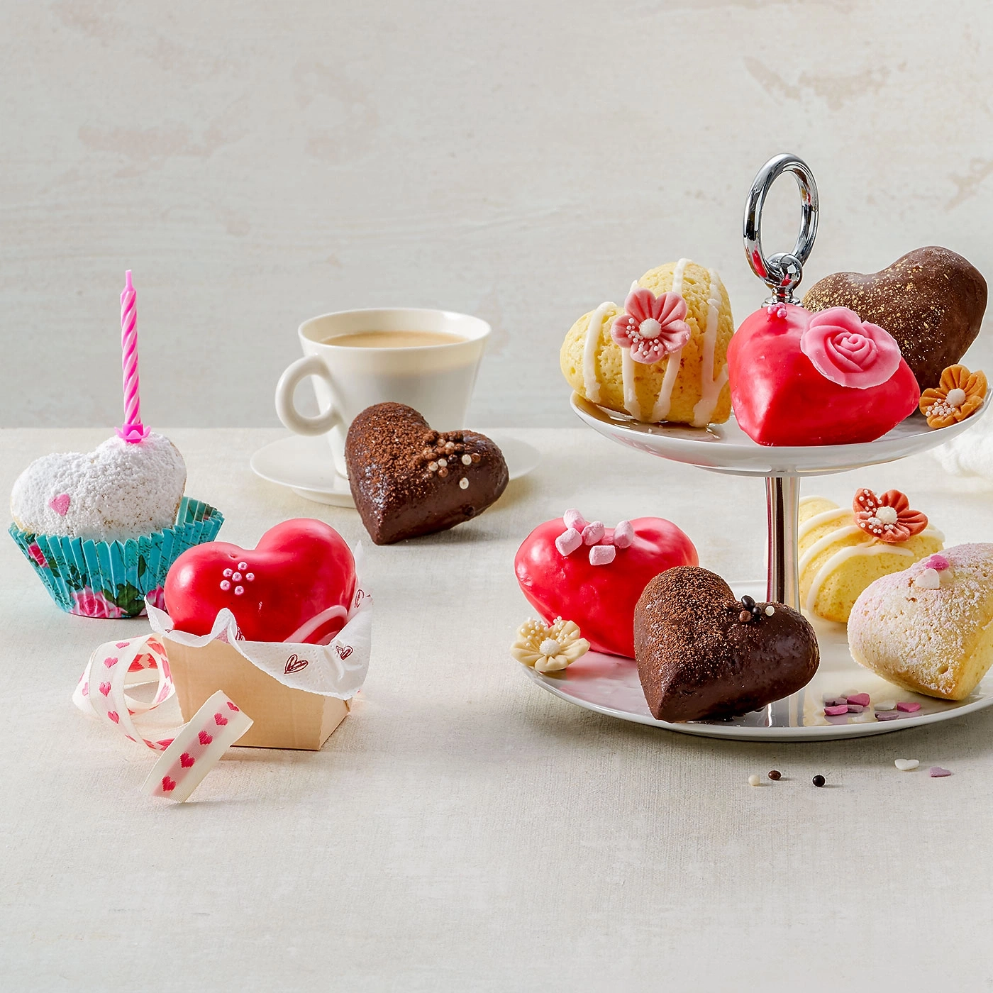 Gâteaux en forme de cœur, cupcakes, café et décorations sur fond clair.