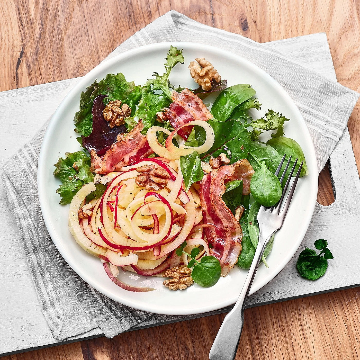 Salat mit Speck, Walnüssen und Zwiebeln auf einem Teller auf Holzuntergrund