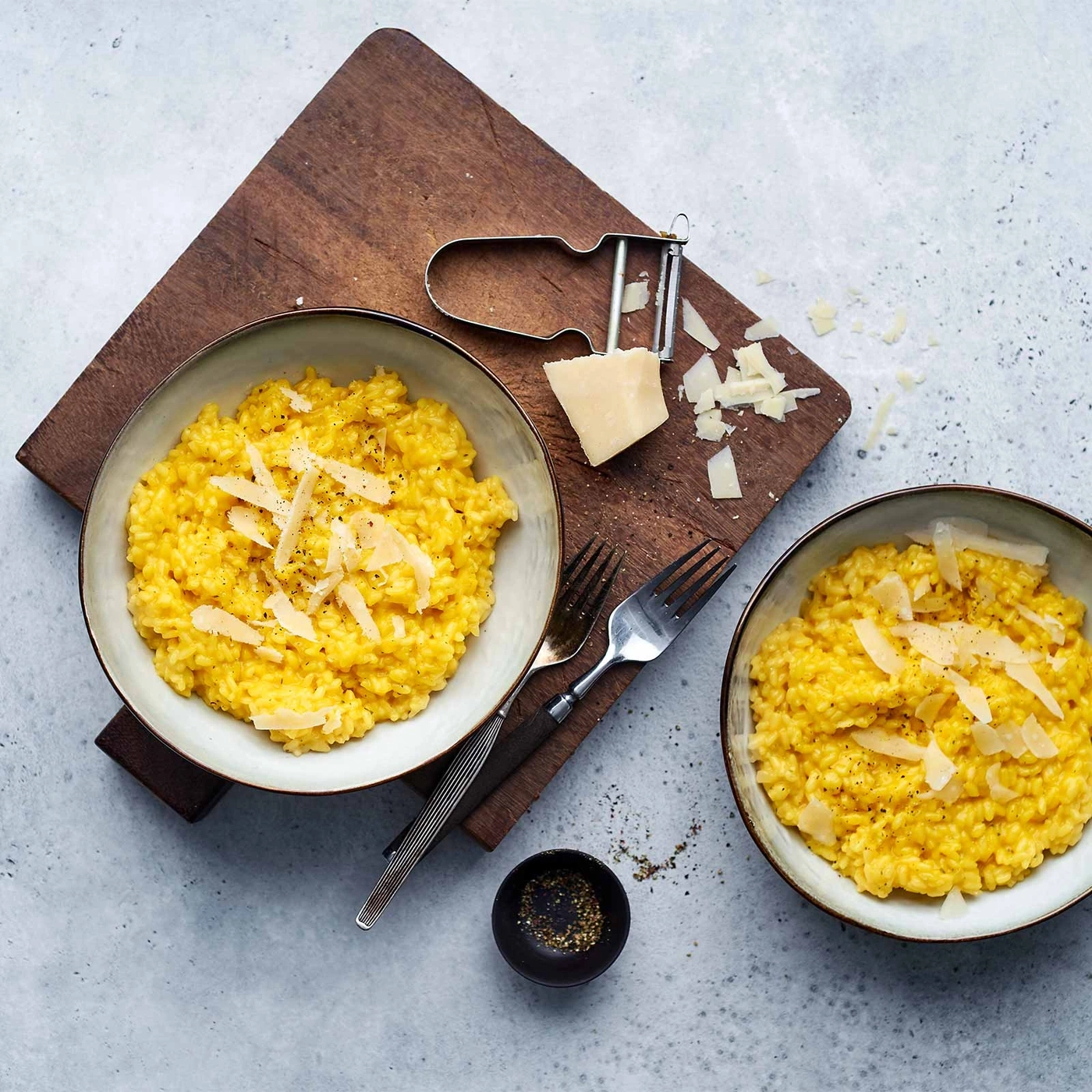 Zwei Schüsseln Risotto mit Parmesan, Gabeln, Pfeffer und Holzbrett.
