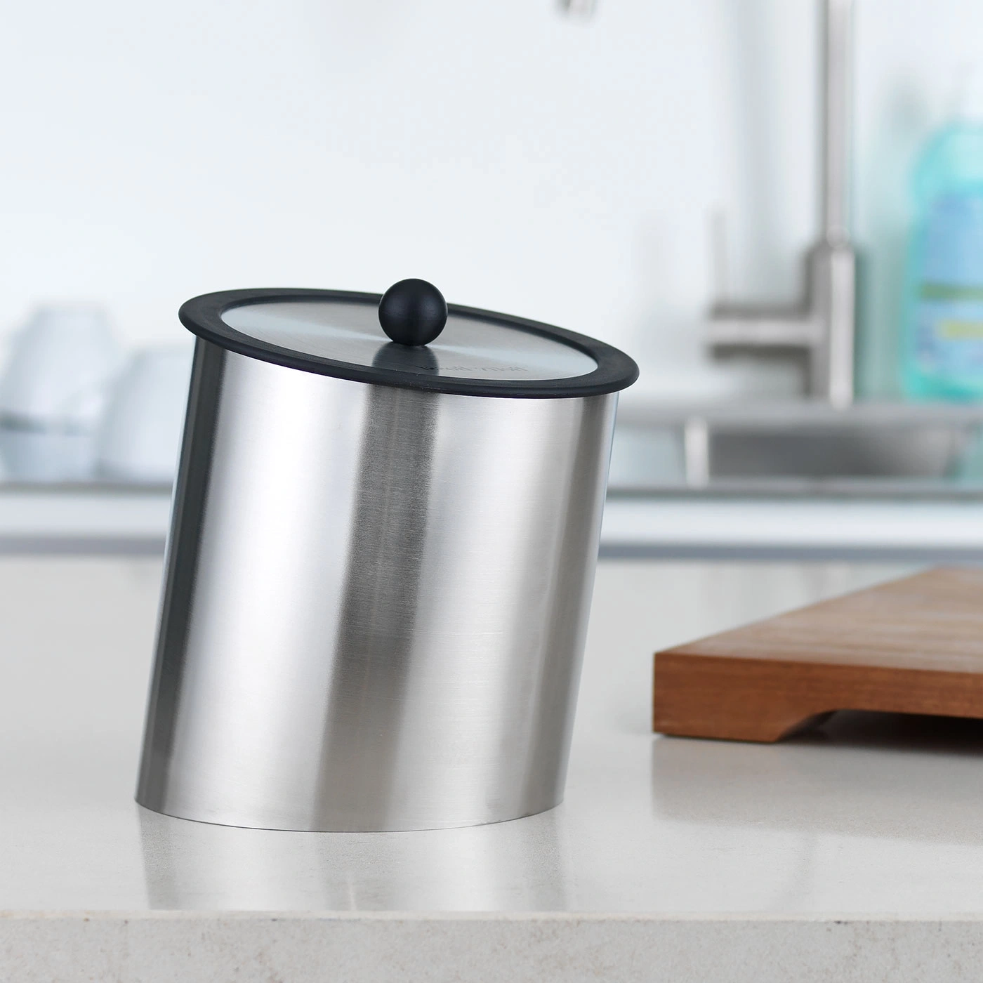 Récipient en acier inoxydable avec couvercle et bouton noir sur un comptoir de cuisine.
