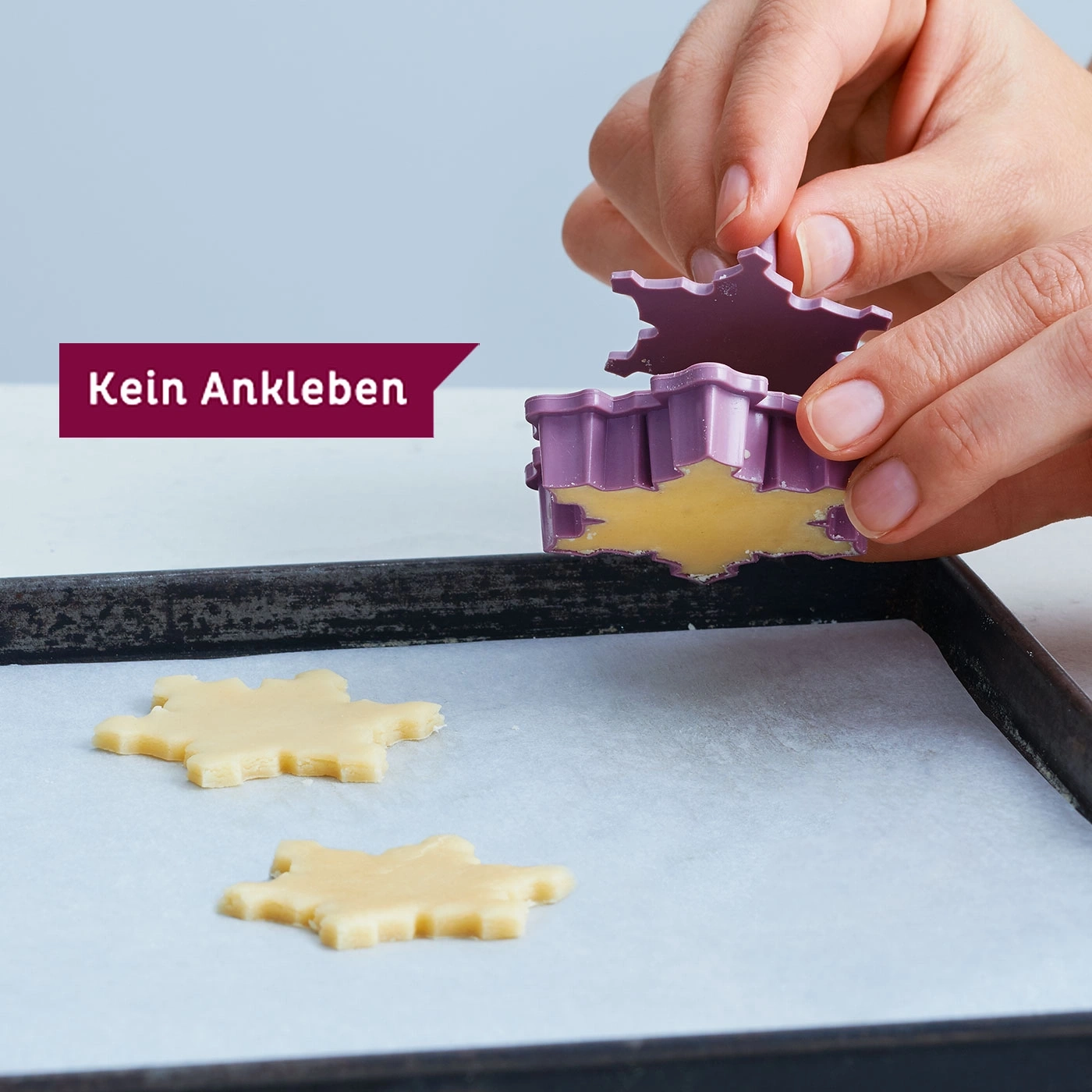 Mains coupant des biscuits avec un emporte-pièce sur du papier sulfurisé. Ne colle pas.