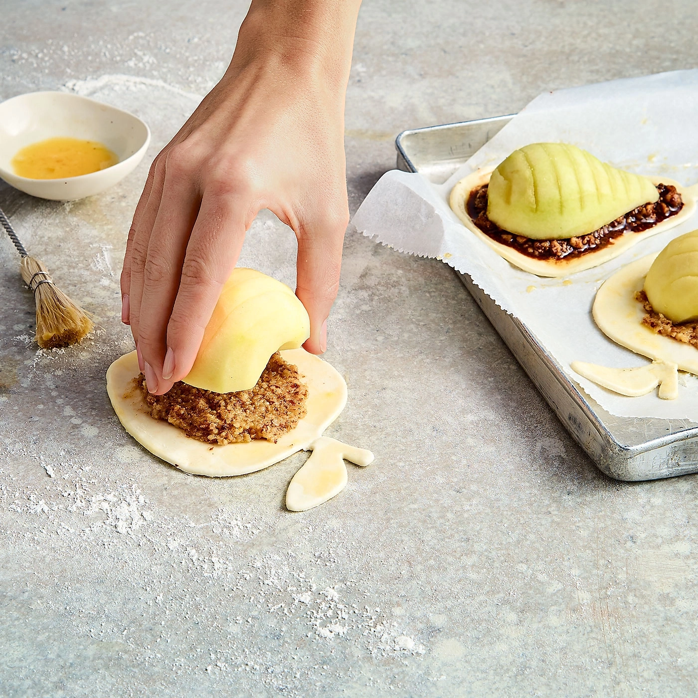 Hand legt Apfel auf Teig mit Füllung, Backblech mit Gebäck, Küche