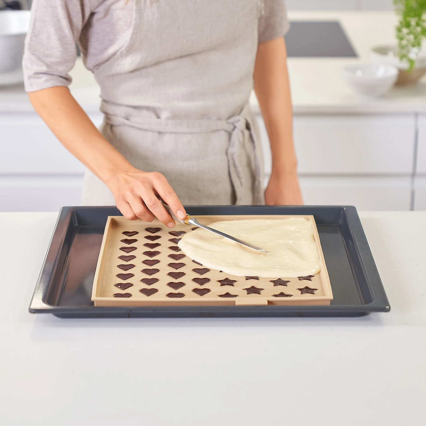 Personne étale pâte sur plaque à pâtisserie avec formes de cœur et d'étoile. Cuisine en arrière-plan.