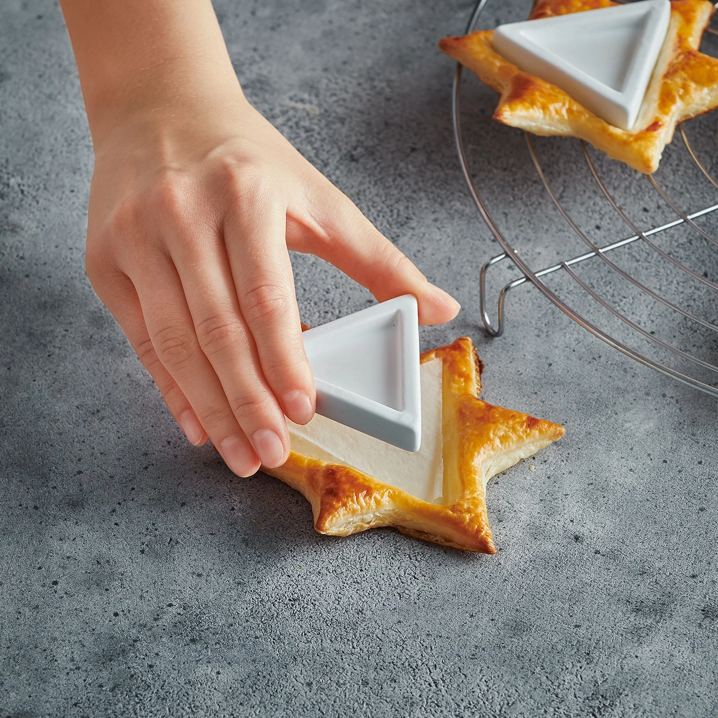 Main plaçant un bol triangulaire sur une pâtisserie en forme d'étoile sur fond gris