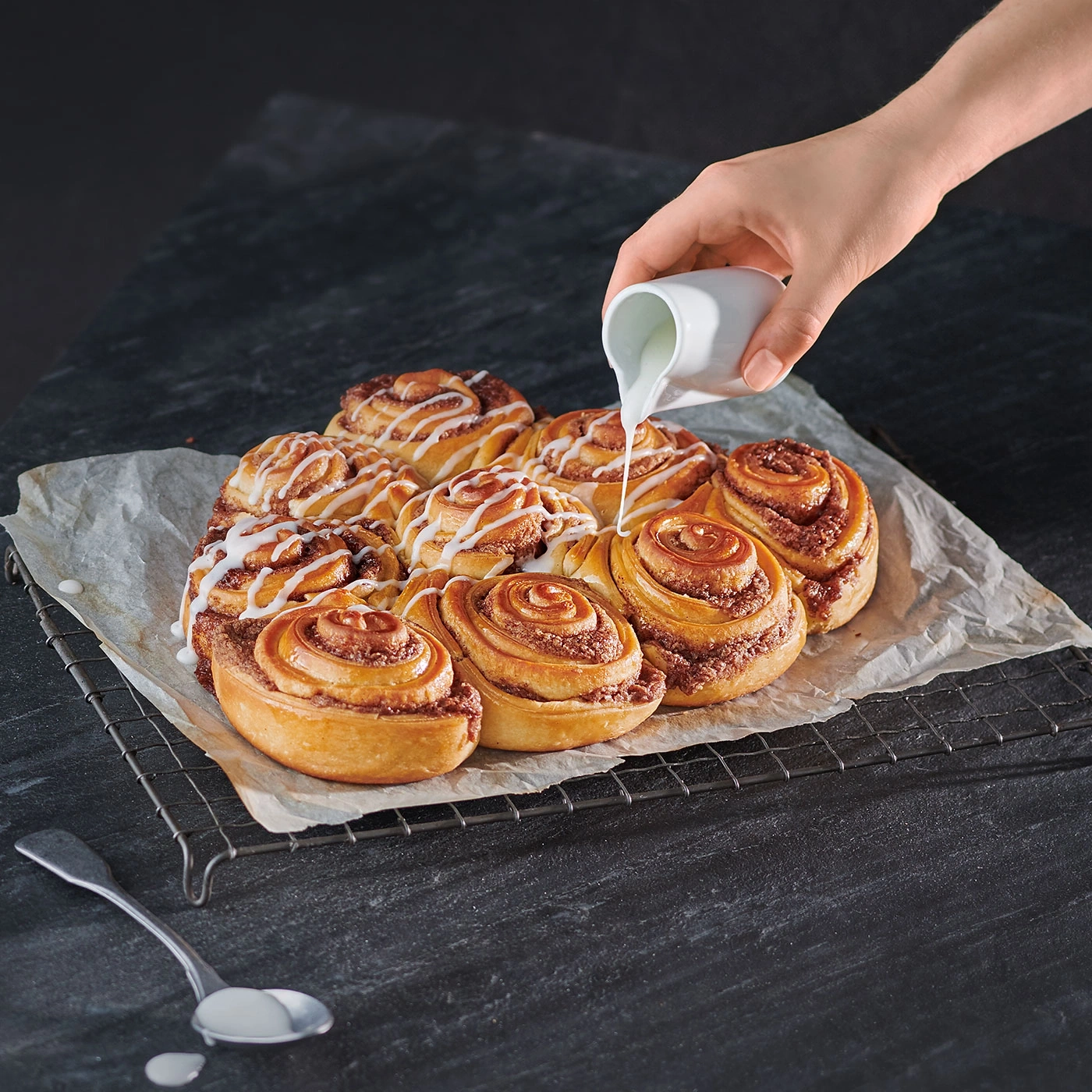 Zimtschnecken mit Zuckerguss, die von einer Hand übergossen werden, auf einem Rost.