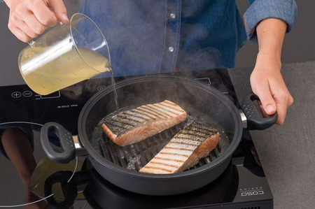 Lachsfilet wird in einer Pfanne gebraten, während Flüssigkeit hinzugefügt wird.