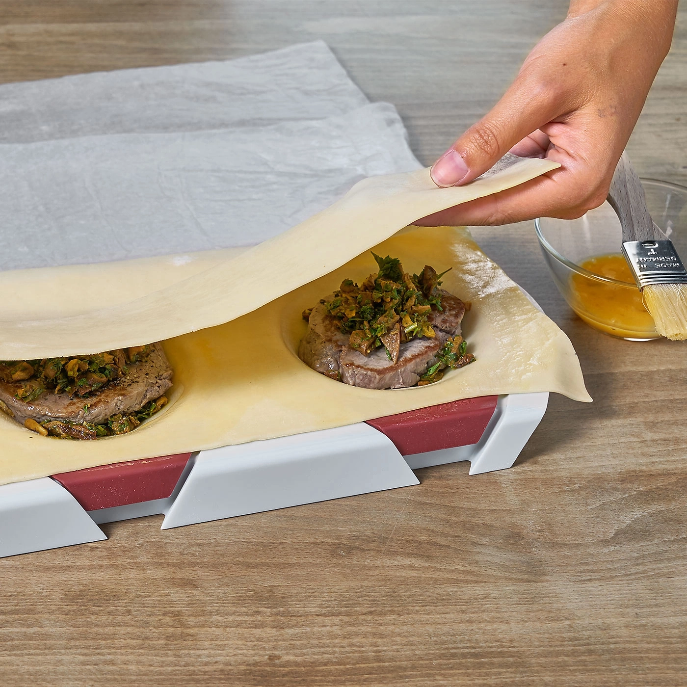 Personne pose de la pâte sur de la viande. Planche en bois, ingrédients et pinceau.
