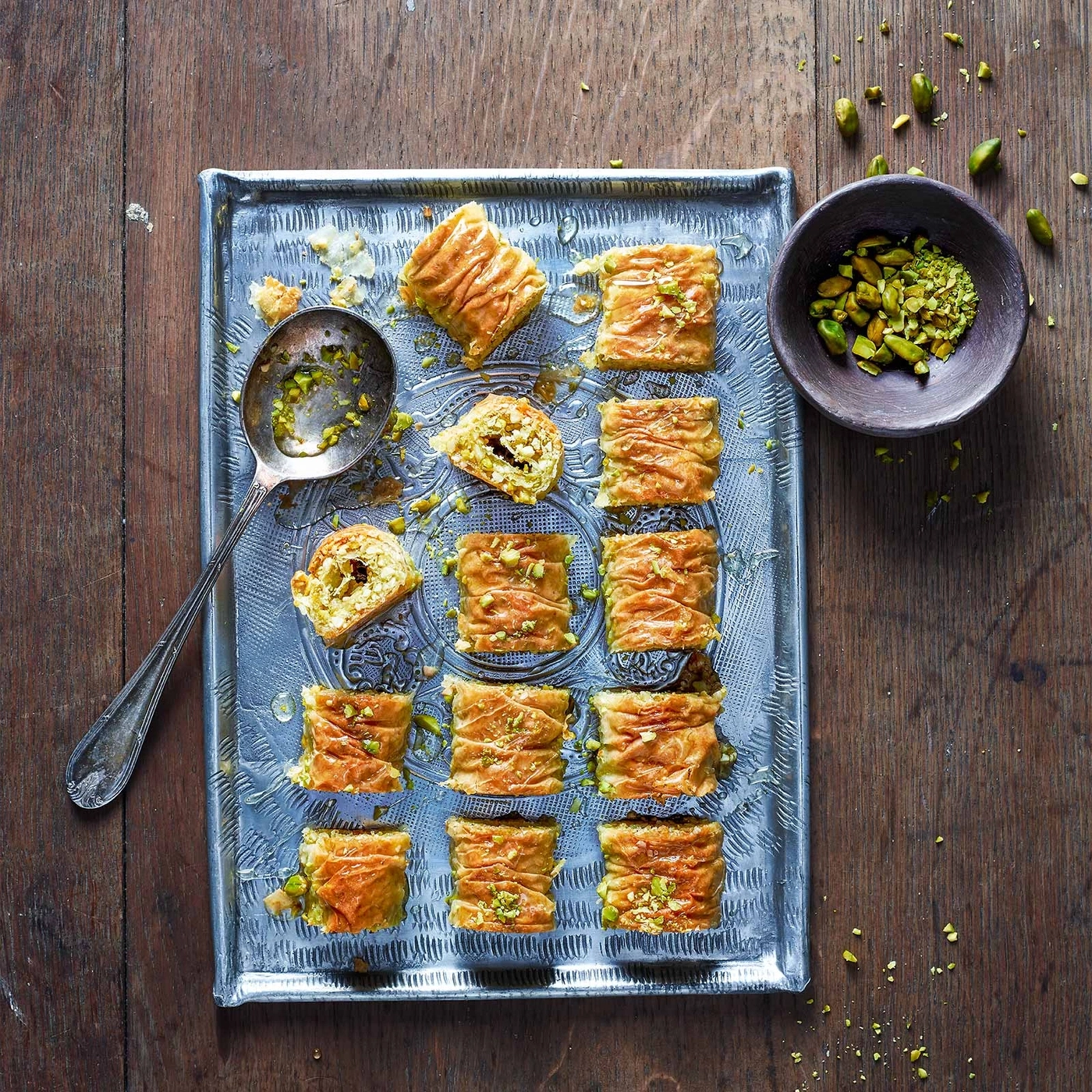 Baklava auf Tablett mit Pistazien, Löffel und Schüssel auf Holz
