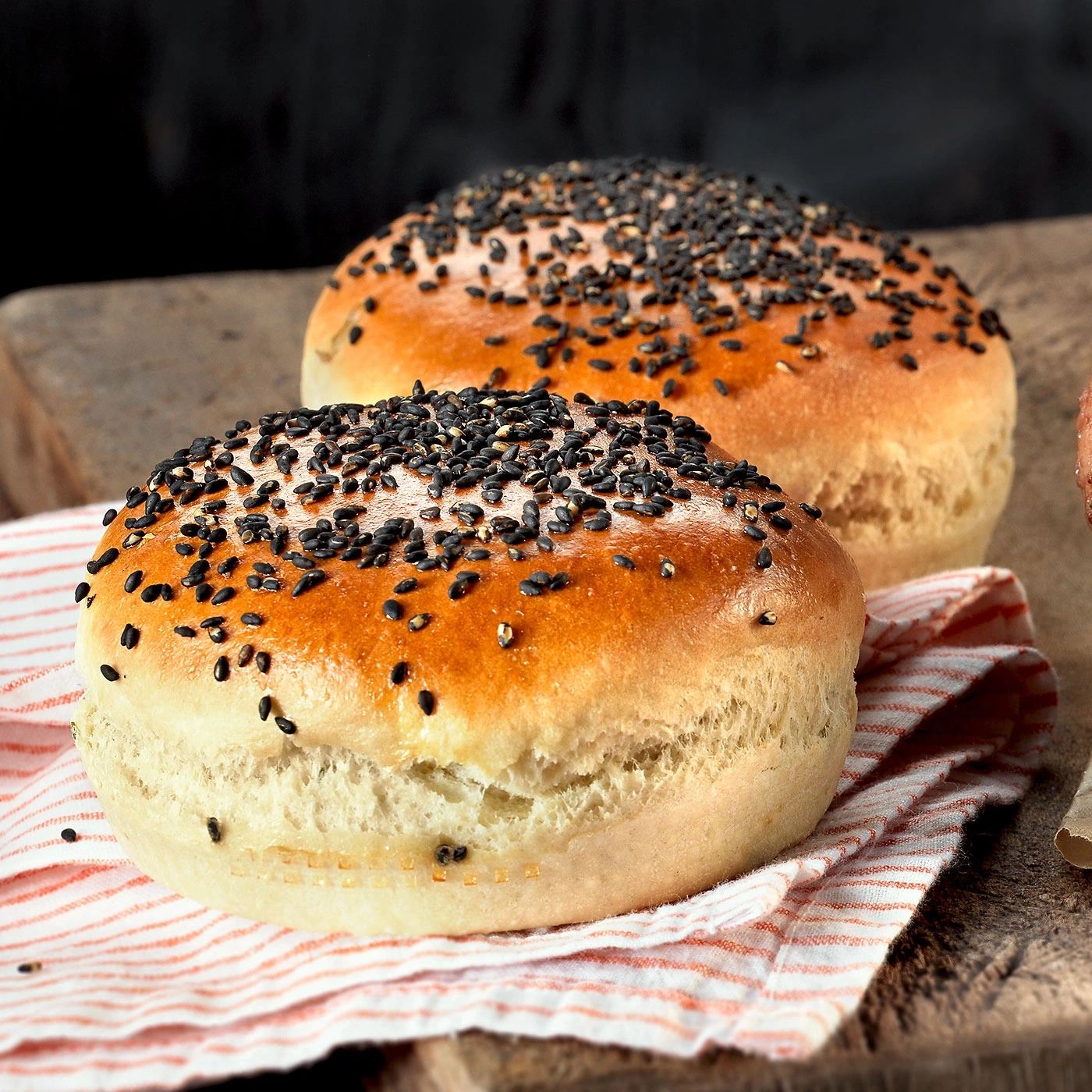 Zwei Brötchen mit Sesam auf einem Holzbrett und einem Tuch