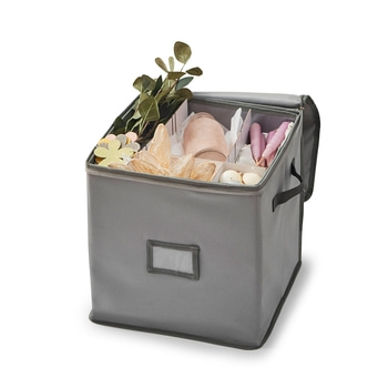 Boîte de rangement grise ouverte avec diverses décorations, poignées visibles.
