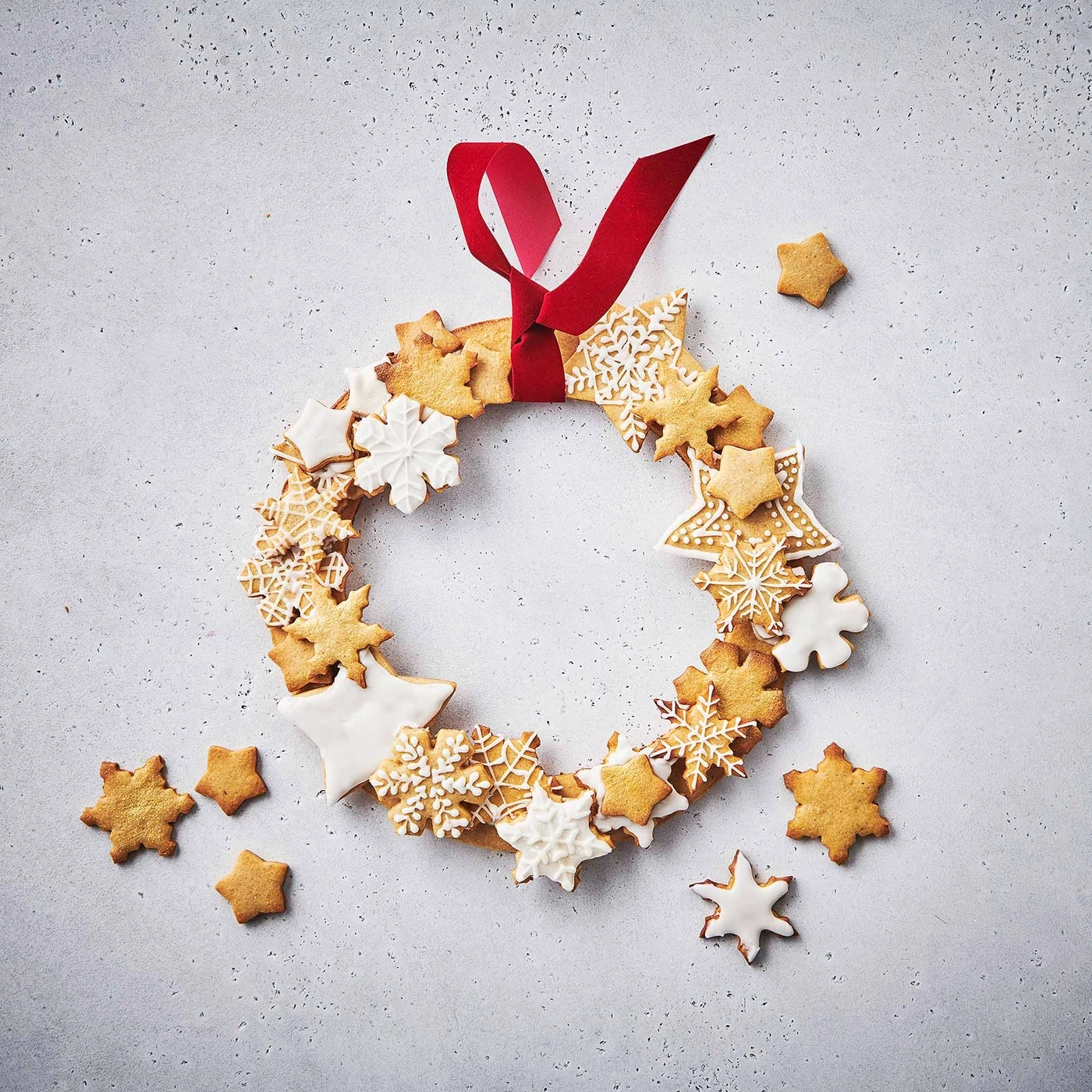 Weihnachtskranz aus Sternkeksen mit rotem Band auf grauem Hintergrund