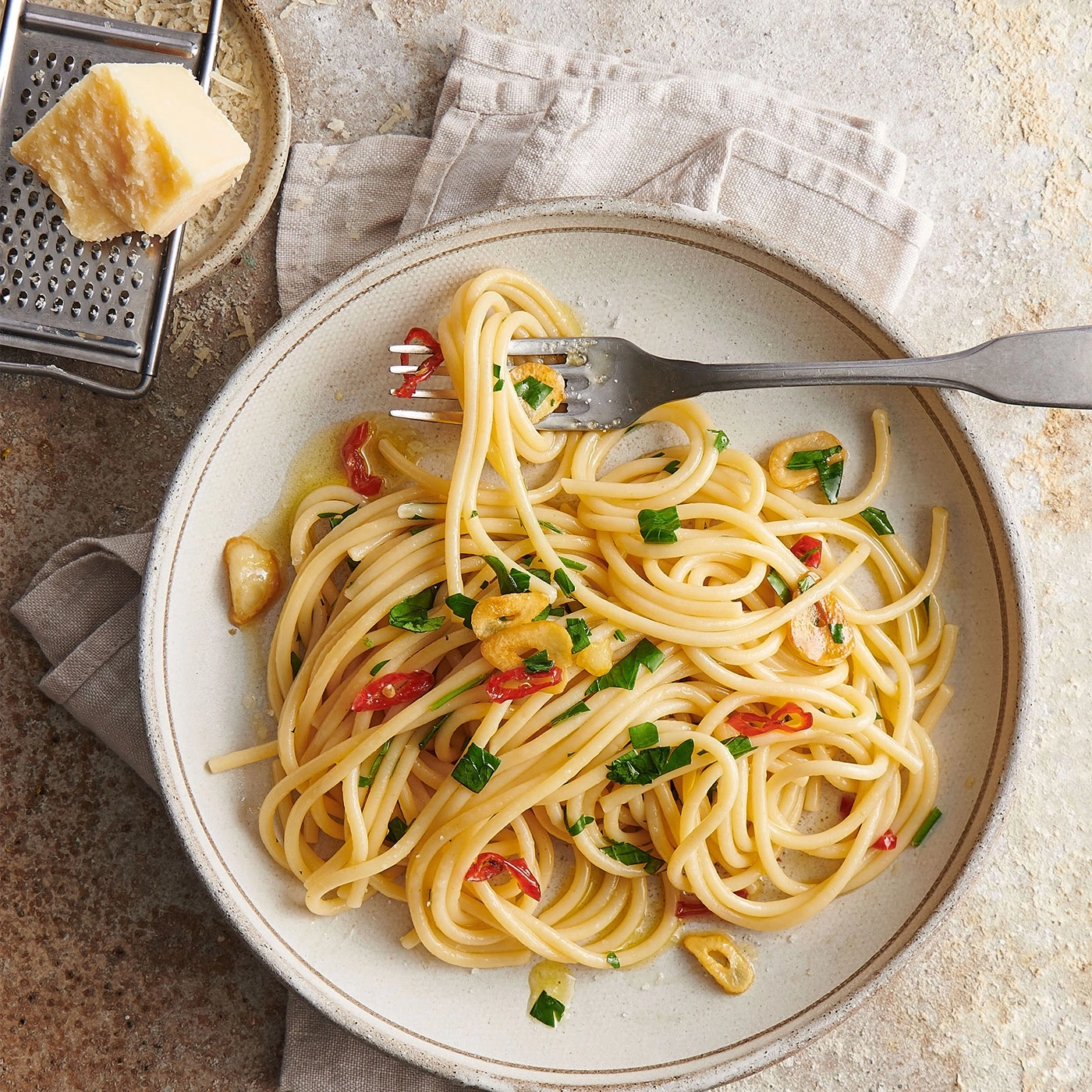 Spaghetti mit Knoblauch, Chili und Petersilie auf einem Teller mit Käse und Reibe