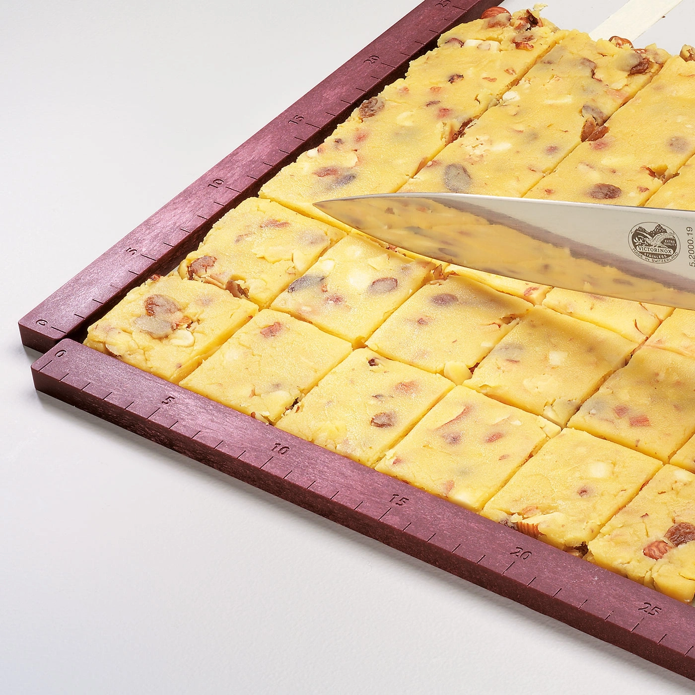 Gâteau coupé en carrés avec un couteau sur une planche à découper.
