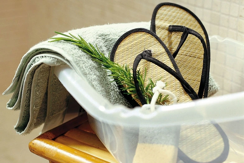 Entspannungs-Set mit Handtuch, Flip-Flops und Kräutern in einer Wanne
