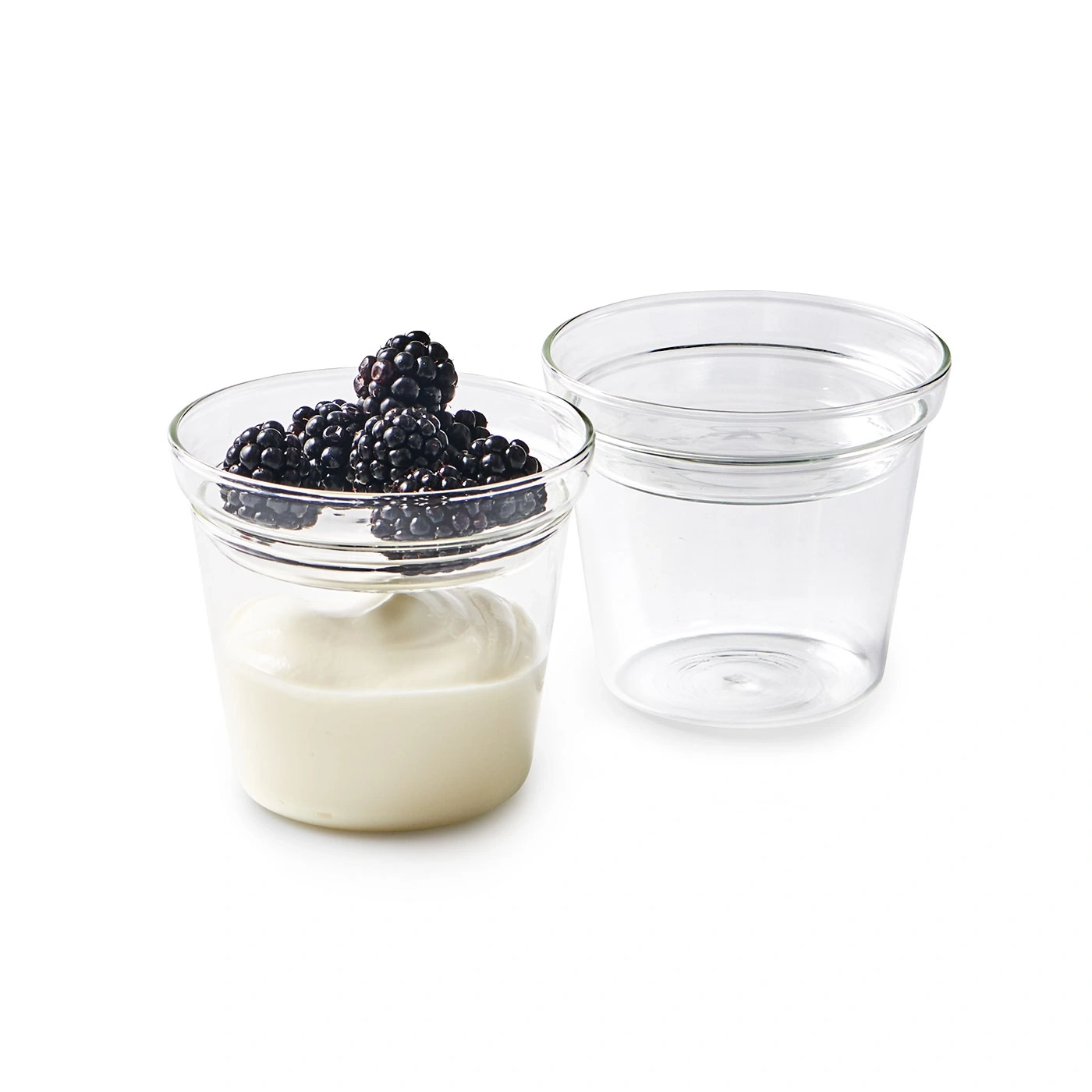 Zwei Gläser, eines mit Joghurt und Brombeeren, das andere leer, auf weißem Hintergrund.
