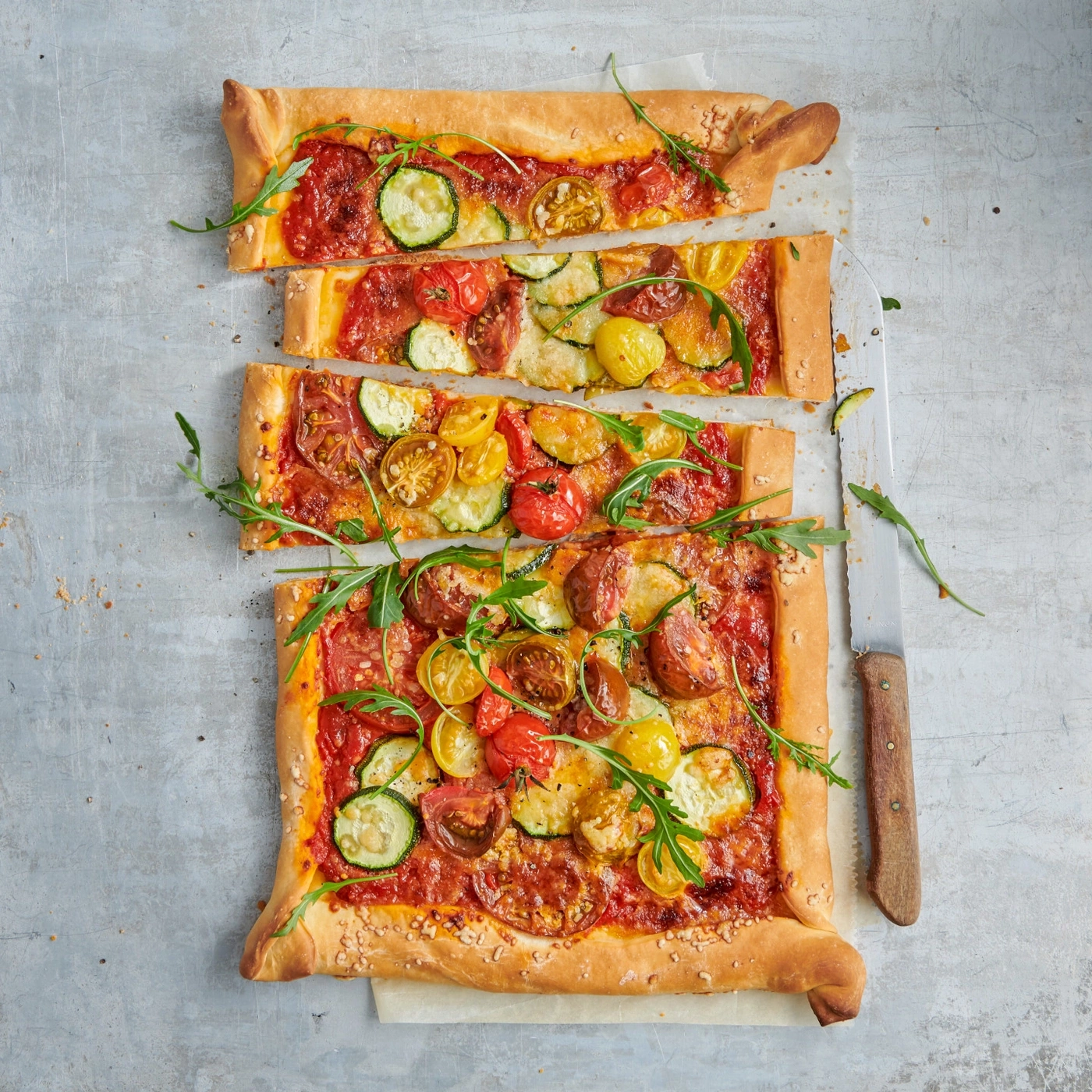 Pizza aux tomates, courgettes et roquette coupée sur fond gris, vue de dessus.