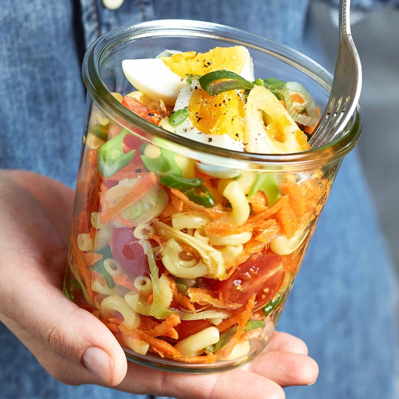 Glas mit Salat, Eiern, Karotten, Tomaten und Nudeln, gehalten von einer Person