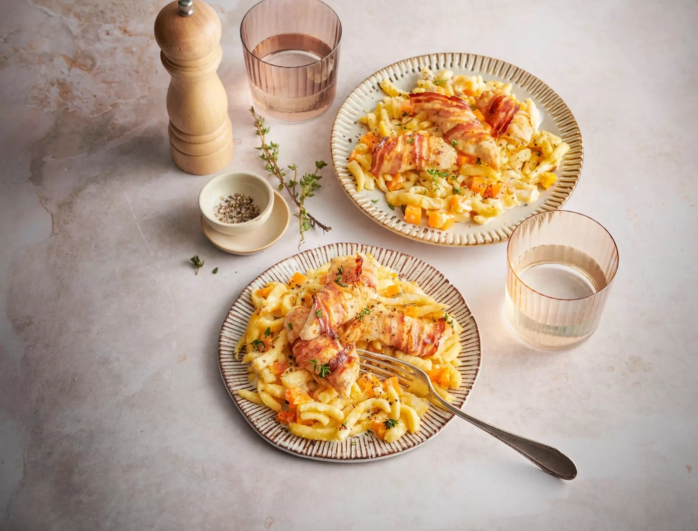 Deux assiettes de pâtes avec poulet enroulé de bacon et citrouille, garnies d'herbes.