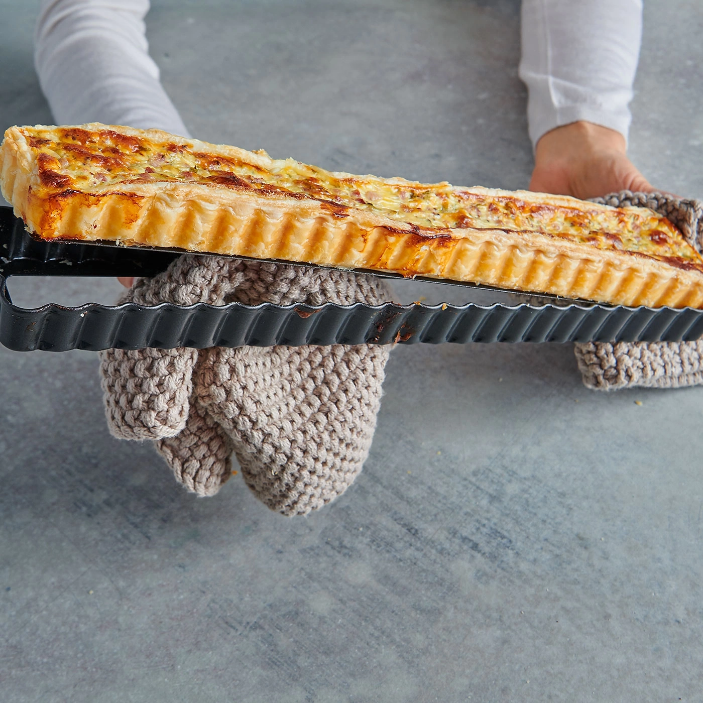 Person hält eine Quiche in einer Backform mit Ofenhandschuhen