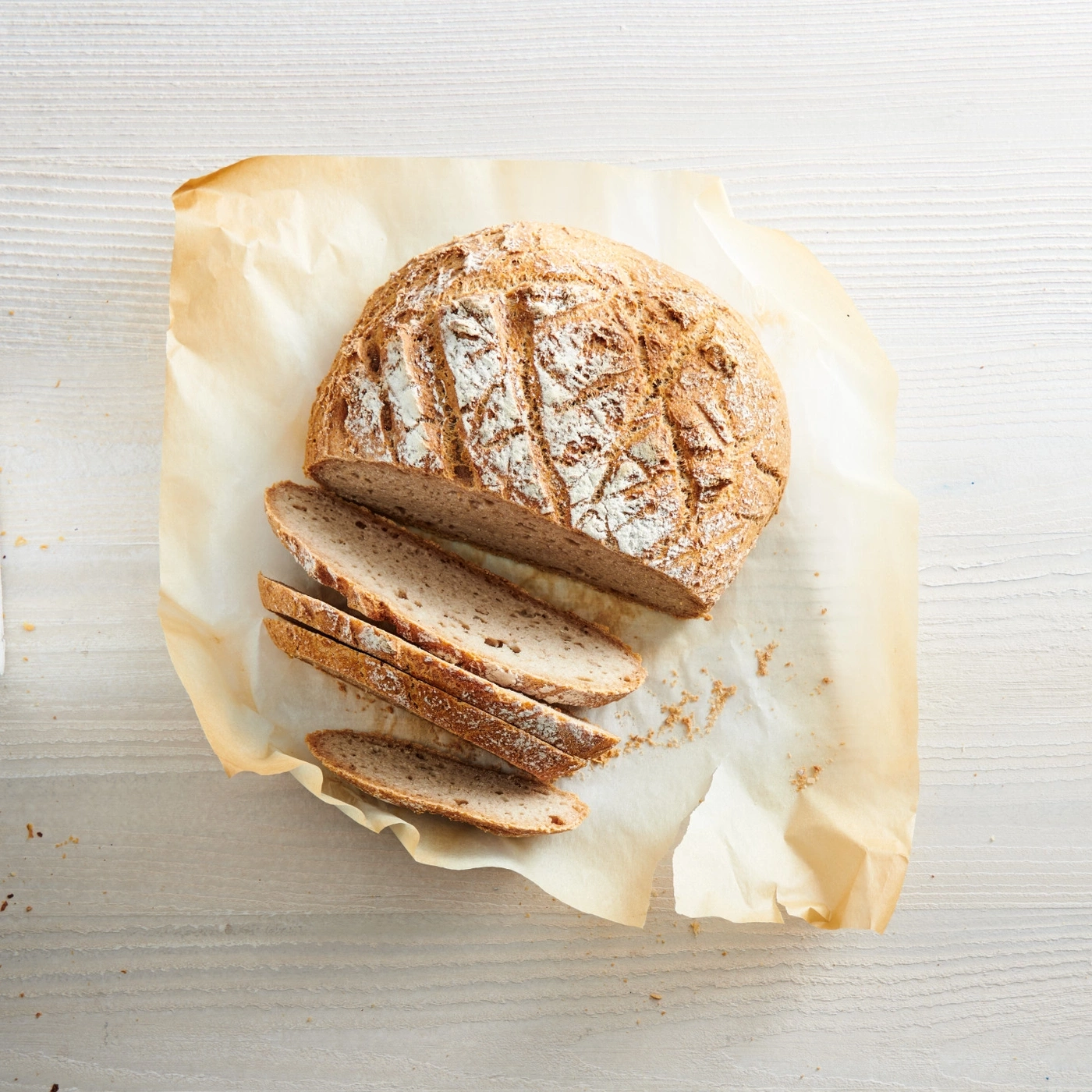 Brot auf Backpapier, geschnitten, auf weißem Holztisch, Nahaufnahme